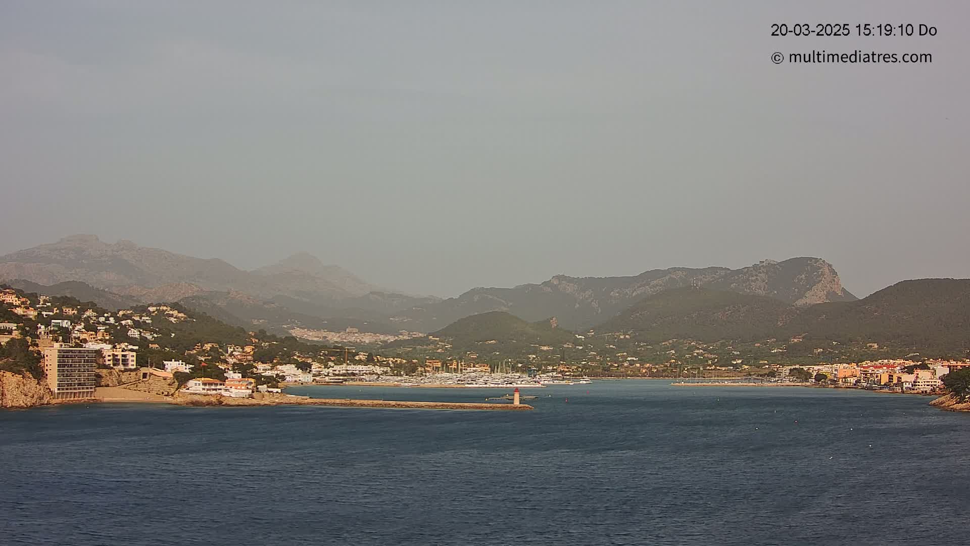 A hazy coastal town nestled between mountains and a calm sea, with a small marina visible.