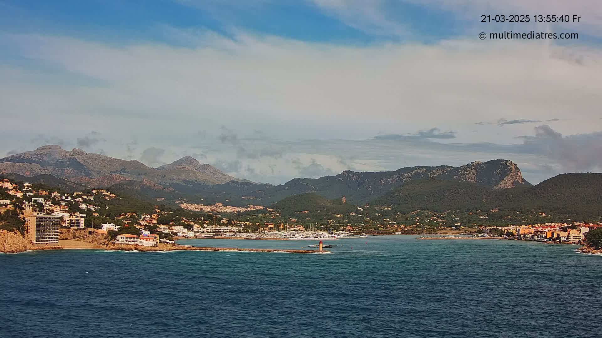 A coastal town nestled between mountains and a calm sea under a partly cloudy sky.