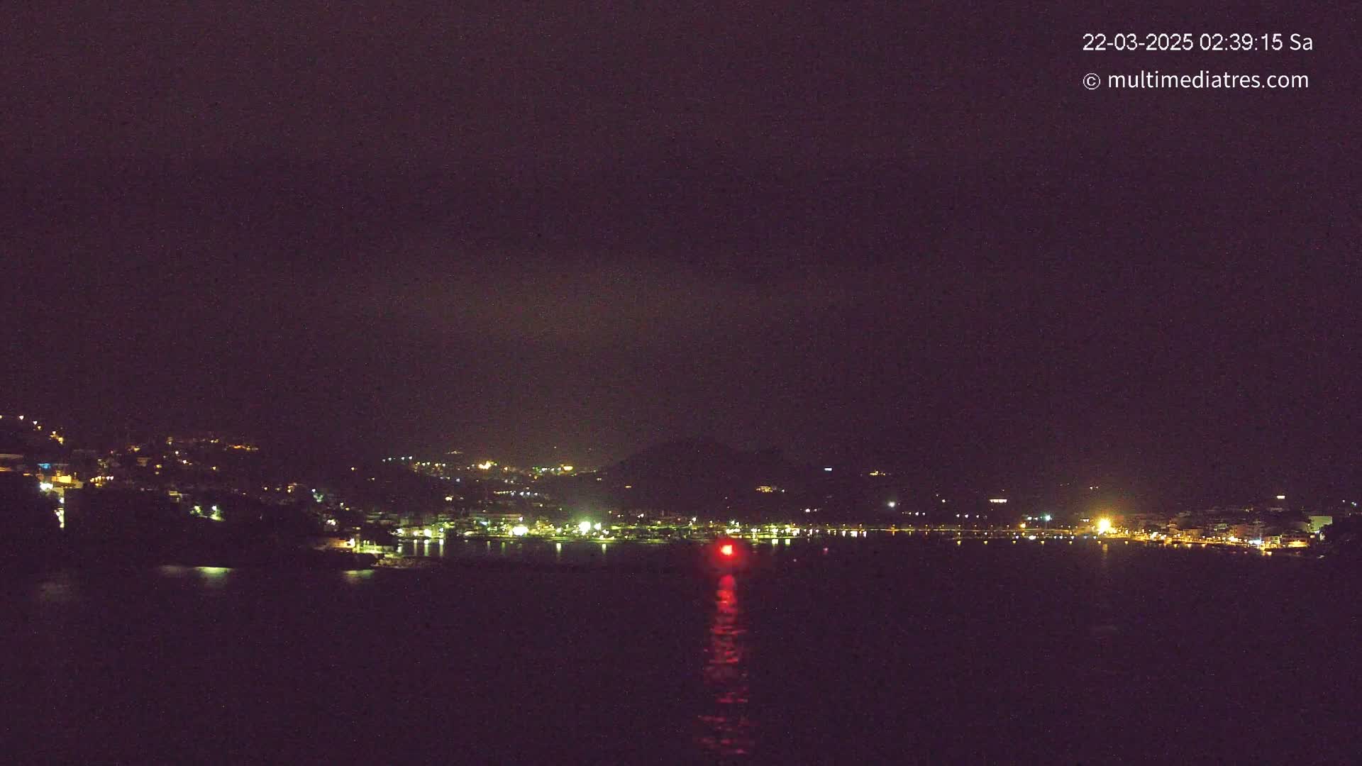 A nighttime view of a coastal town's lights across a dark body of water under a mostly clear, dark sky.