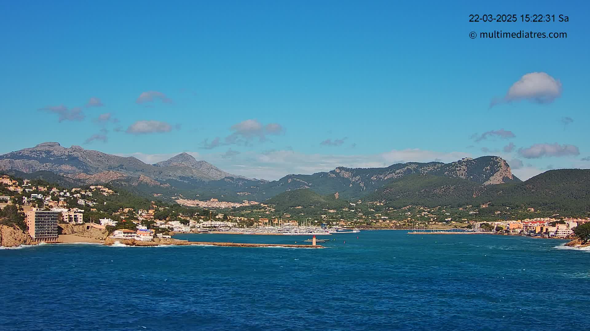 A coastal town nestled between a marina and mountains under a mostly clear blue sky.