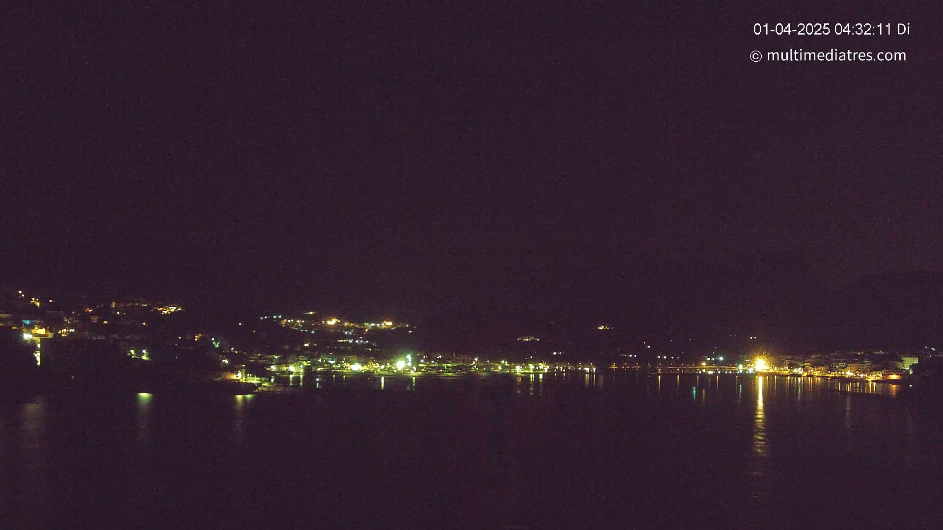 A nighttime view of a city's lights along a dark body of water under a clear, starless sky.