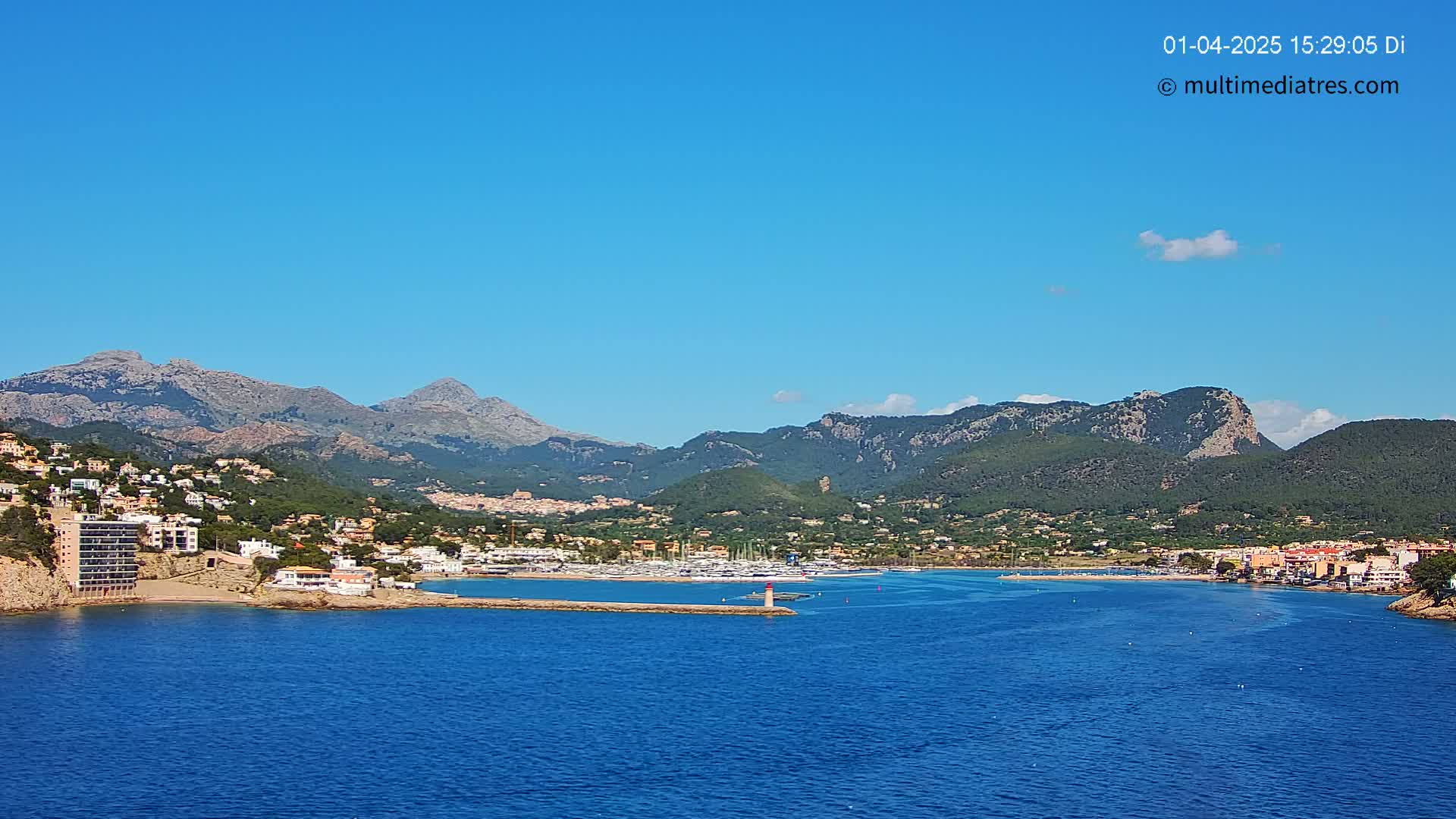A coastal town nestled between mountains and a calm blue sea under a clear blue sky.