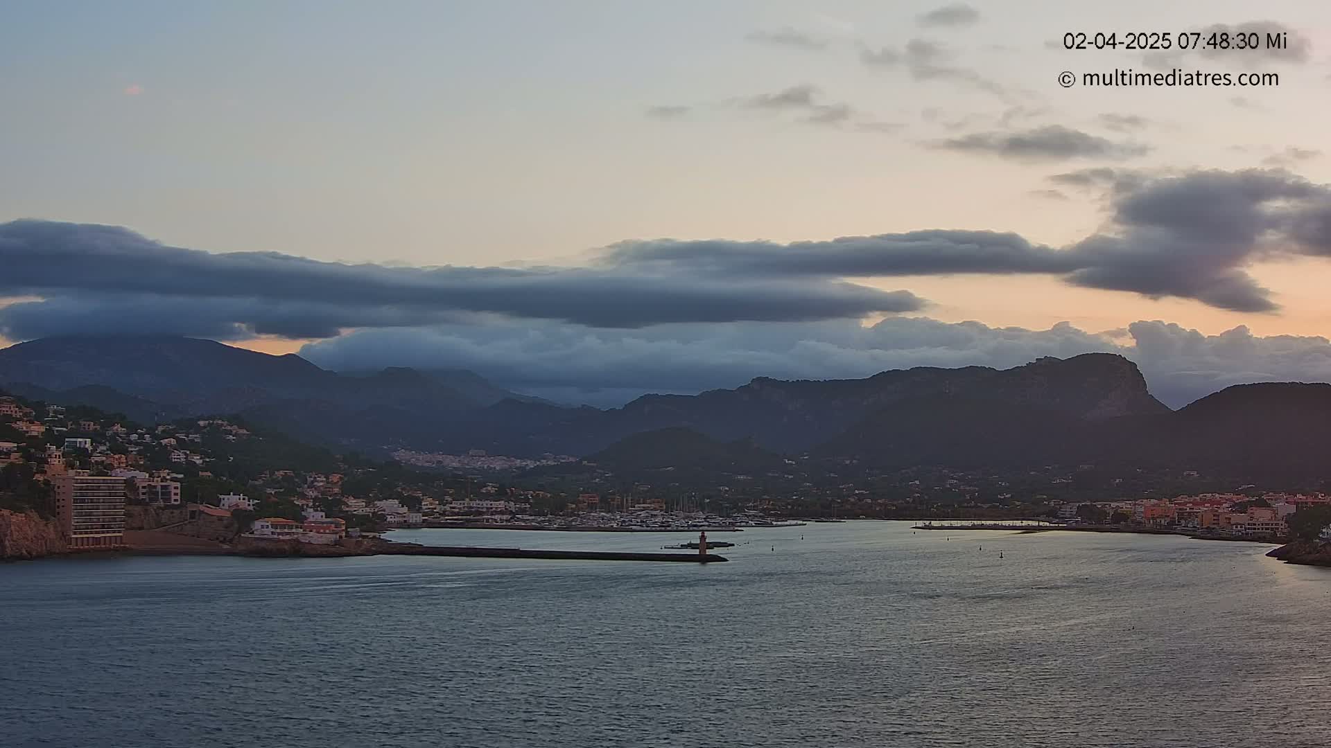 A coastal town nestled between dark mountains is partially shrouded by low-hanging clouds under a dusky sky.