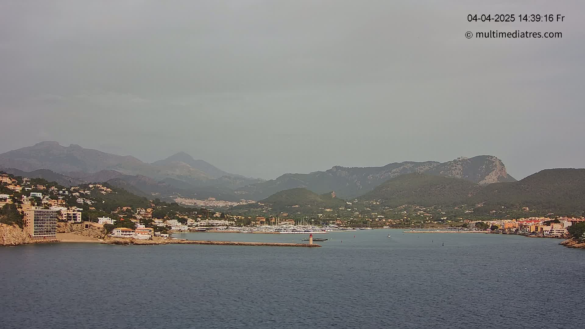 A hazy coastal town nestled between mountains and a calm sea, with a marina filled with boats.