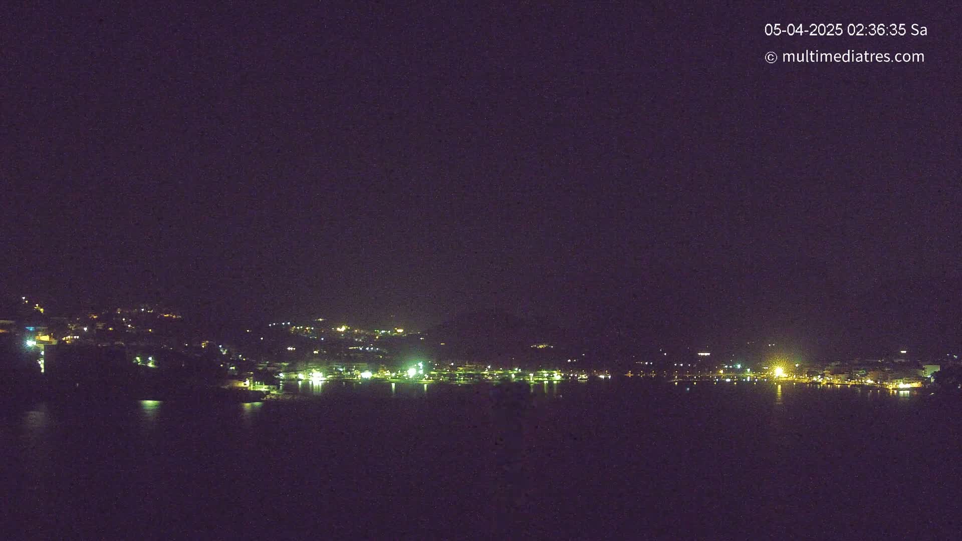 A nighttime view of a town situated along a body of water, under a clear, dark sky.