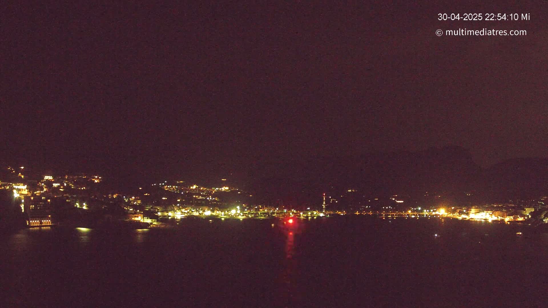 A nighttime view of a city's lights spread across a hillside and along a dark body of water.