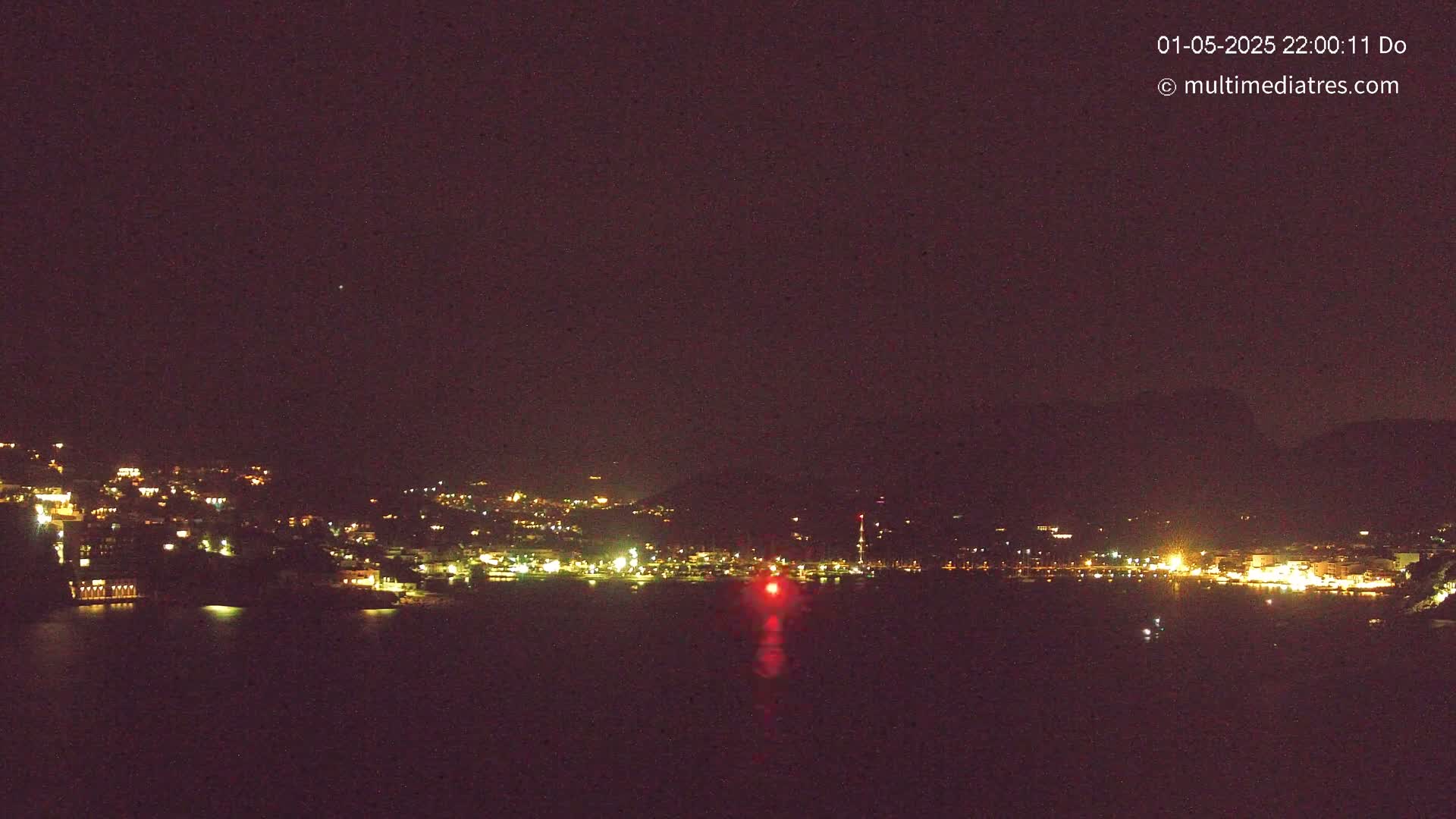 A nighttime view of a town's lights across a dark body of water under a clear, dark sky.