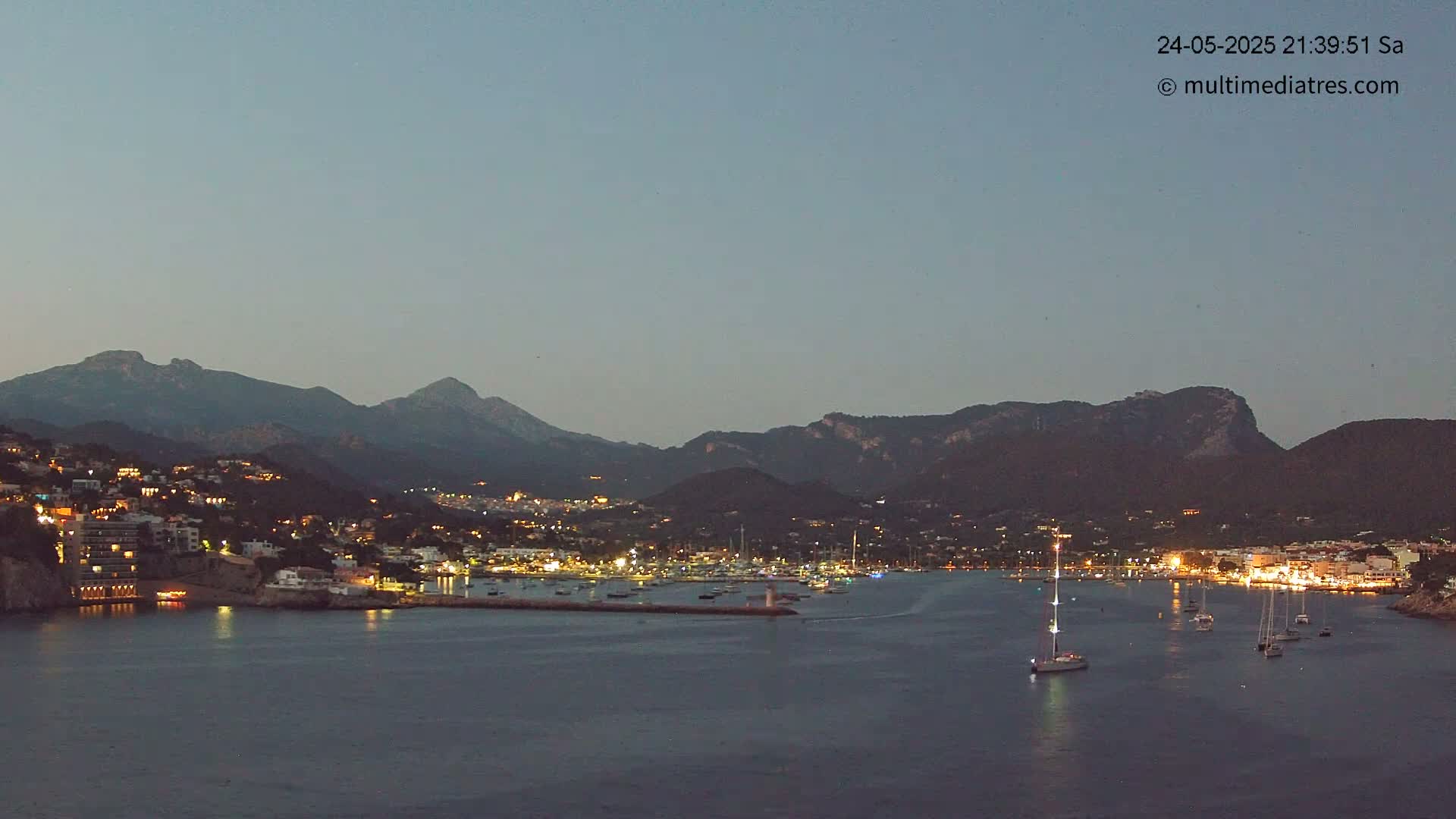 A nighttime view of a harbor town nestled beside mountains under a twilight sky.