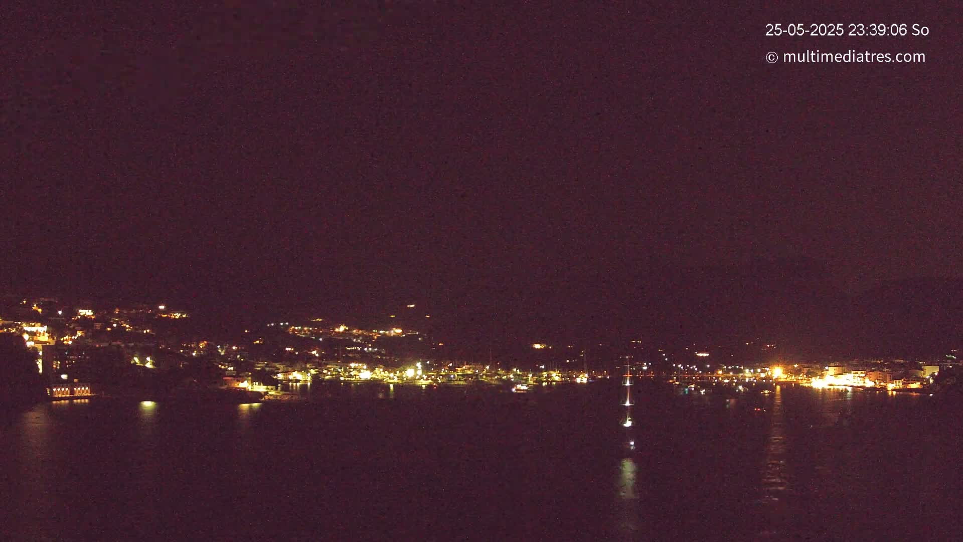 A nighttime view of a coastal town with its lights illuminating the dark water, under a clear, dark sky.