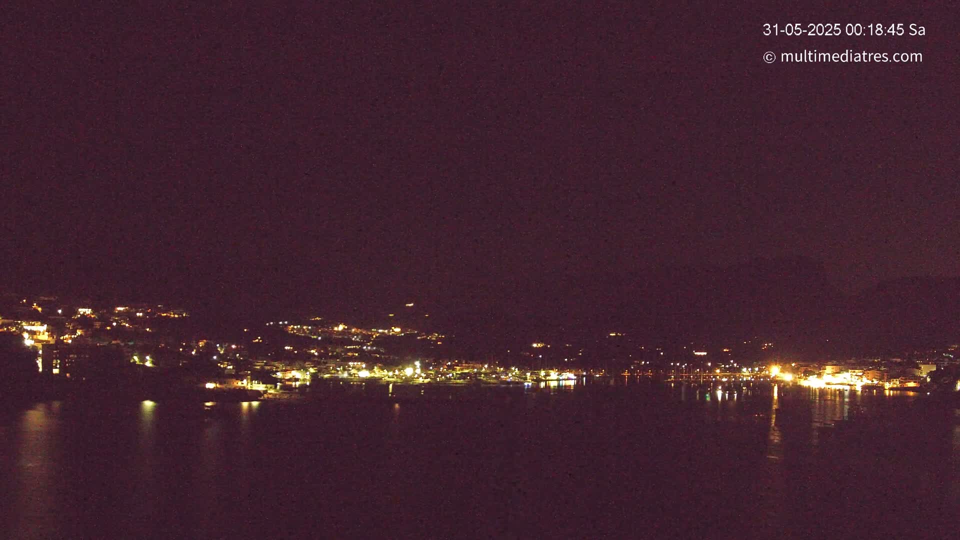 A nighttime view of a city's lights across a dark body of water under a clear, dark sky.