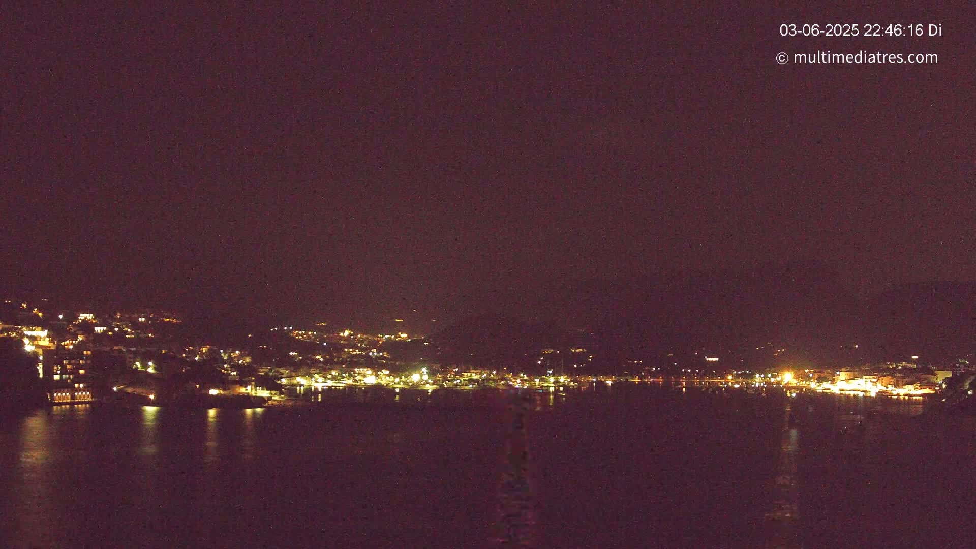 A nighttime view of a town's lights across a dark body of water under a clear, dark sky.