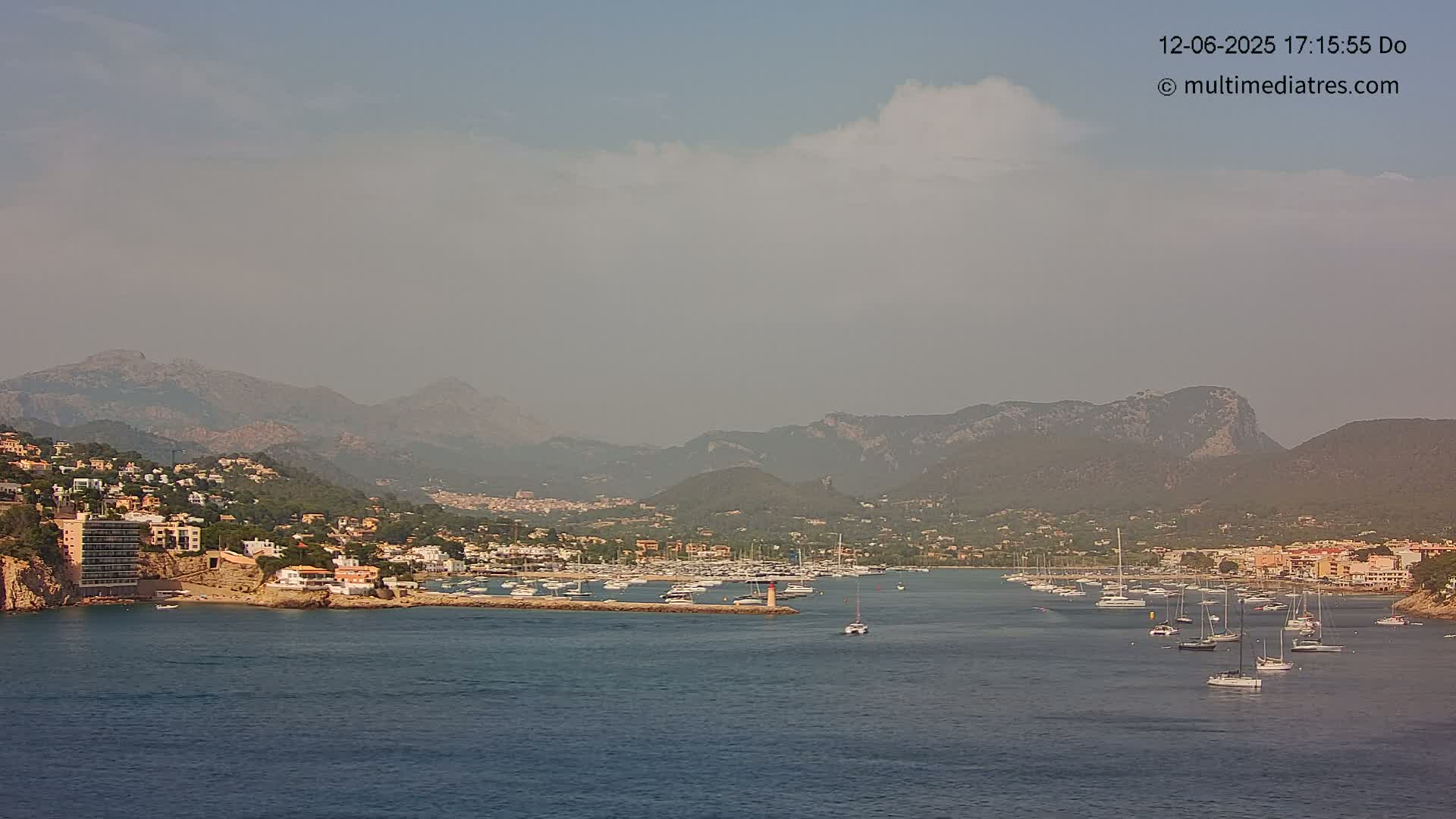 A hazy coastal town nestled between mountains and a calm bay filled with sailboats.