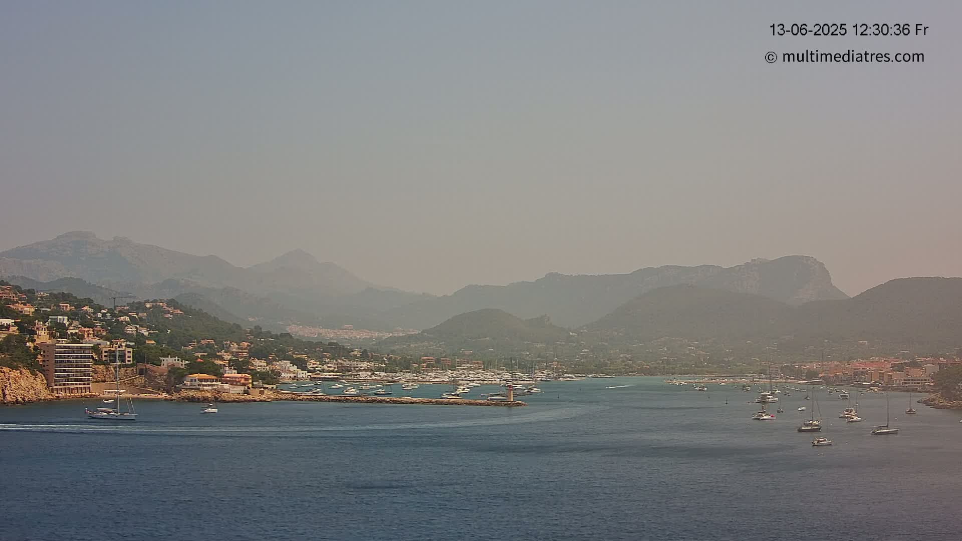 A hazy coastal town with a marina nestled between mountains and a calm sea.