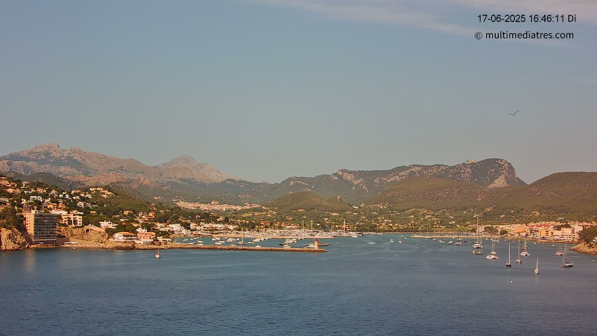 A coastal town nestled between mountains, with a harbor filled with boats, under a clear, hazy sky.
