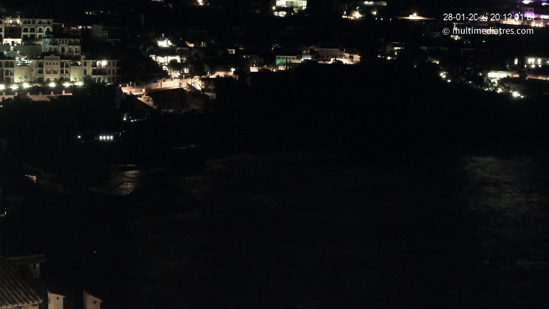 A nighttime long shot shows a coastal town with scattered lights, overlooking a dark body of water.
