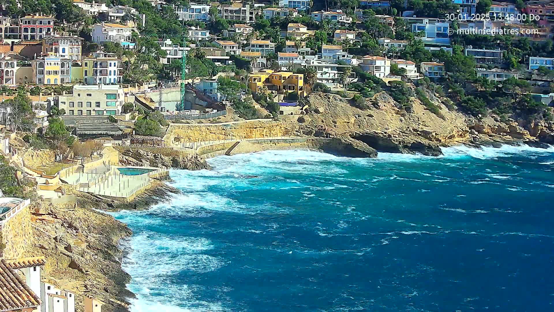 A rocky coastline with a cluster of buildings overlooks a choppy, blue sea.