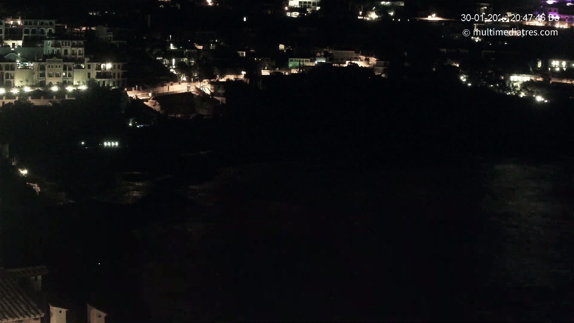 A nighttime view of a coastal town with buildings illuminated against a dark body of water.