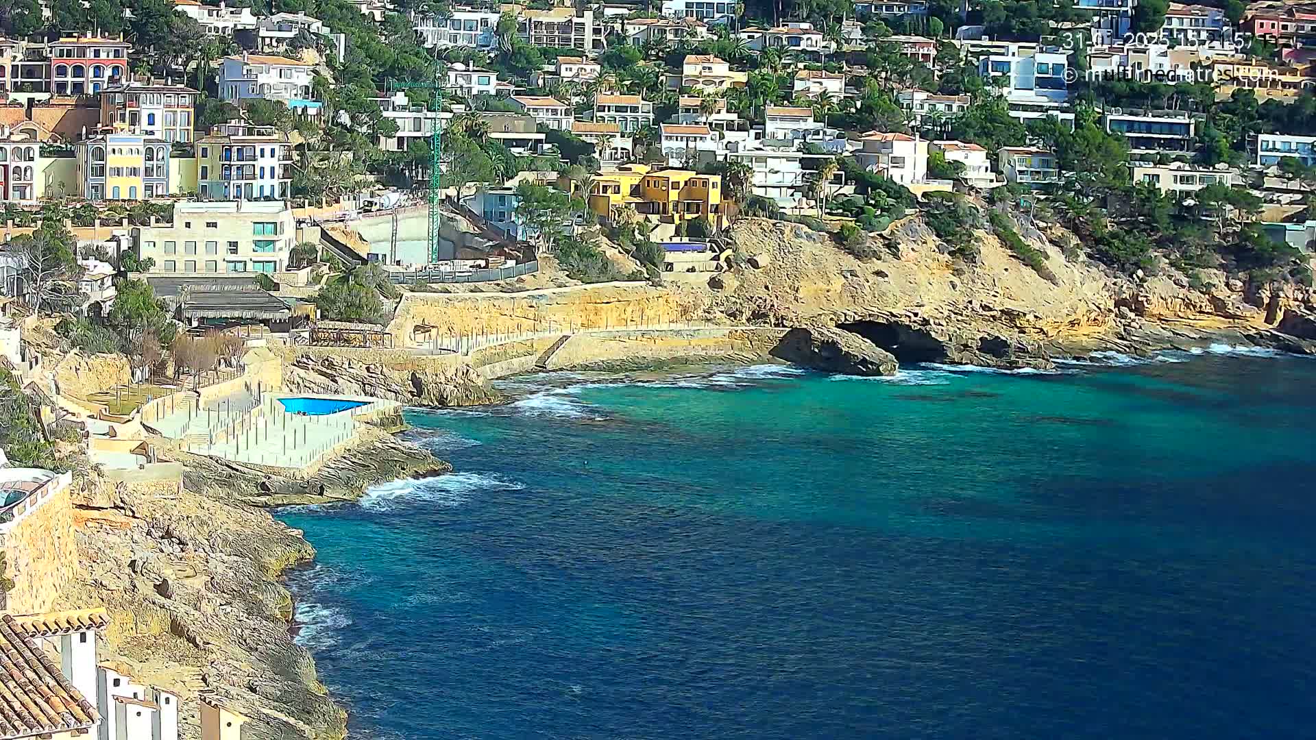 A coastal town with colorful buildings is nestled on a rocky hillside overlooking a clear, turquoise sea under sunny skies.