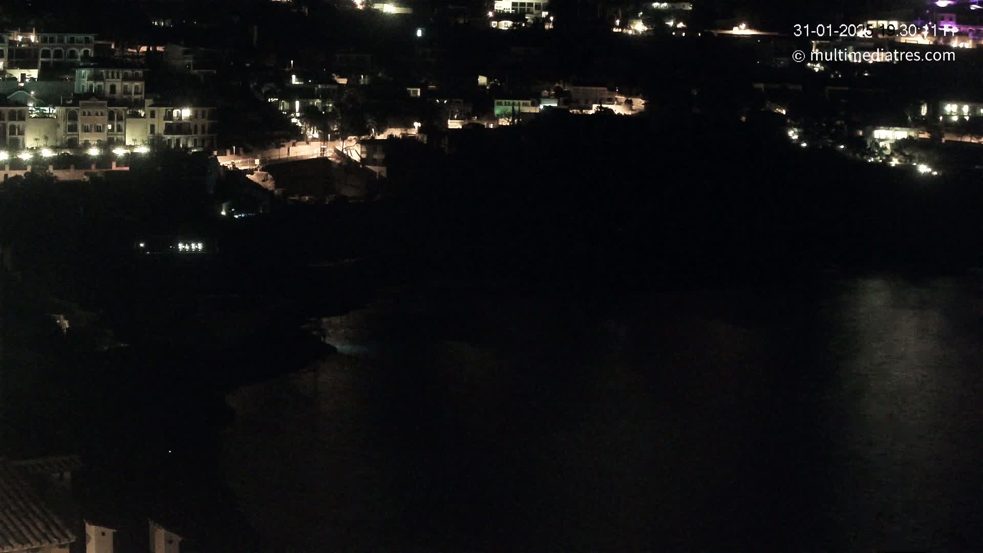 A nighttime view of a coastal town with dimly lit buildings and a dark body of water.