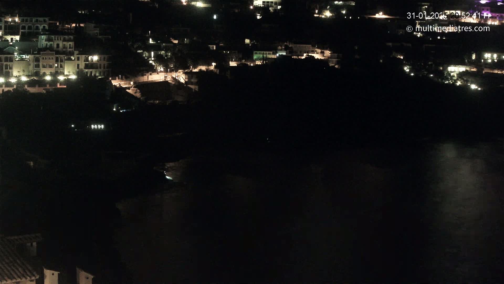 A nighttime view of a coastal town with its lights illuminating the buildings and a dark body of water below.
