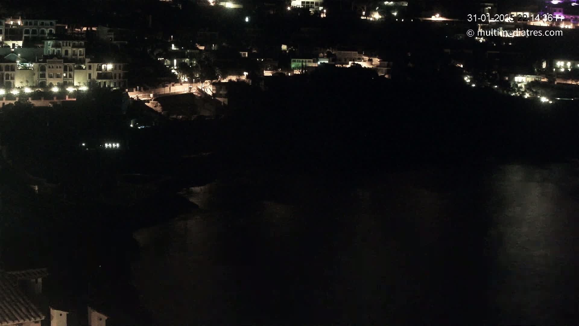 A nighttime view of a coastal town with buildings illuminated against a dark body of water.