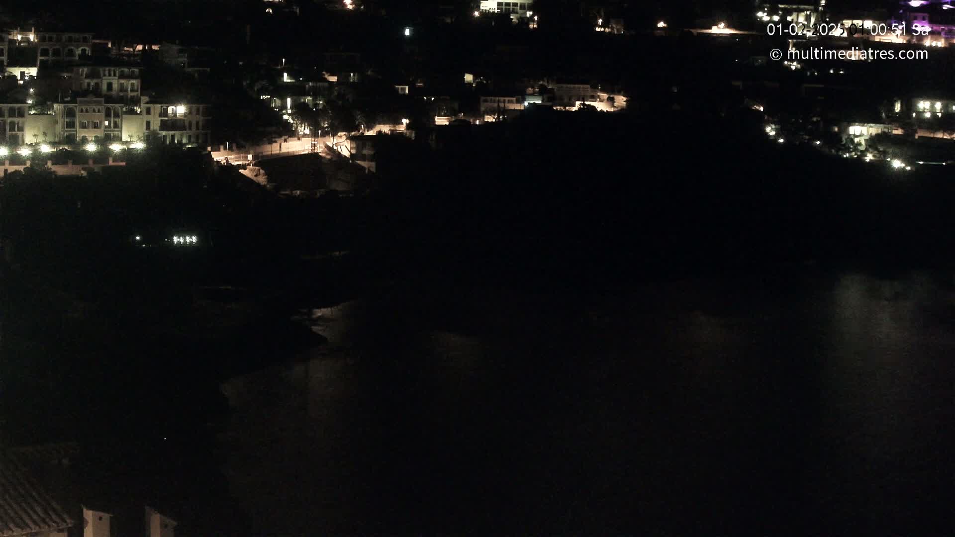 A nighttime view of a coastal town with buildings illuminated against a dark body of water.