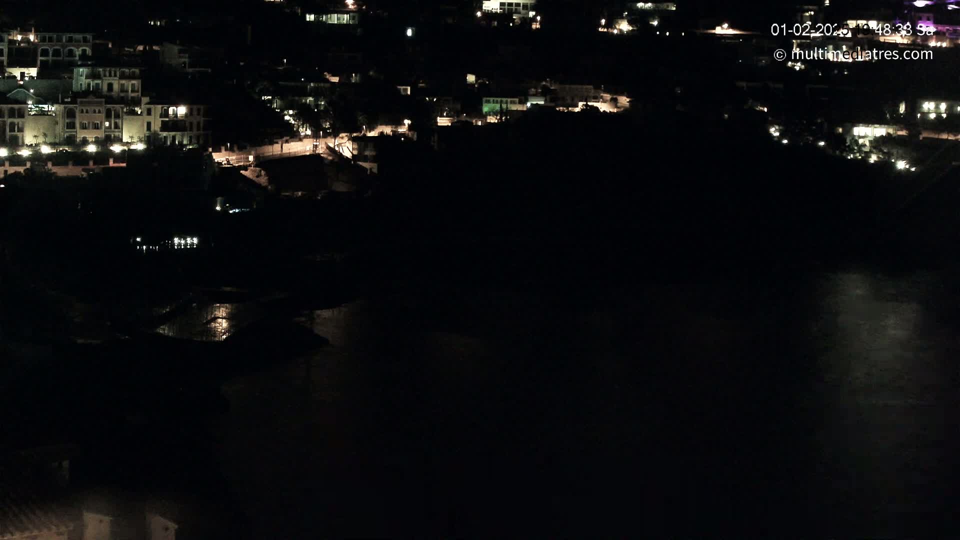 A nighttime view of a coastal town with dimly lit buildings and a dark body of water below.