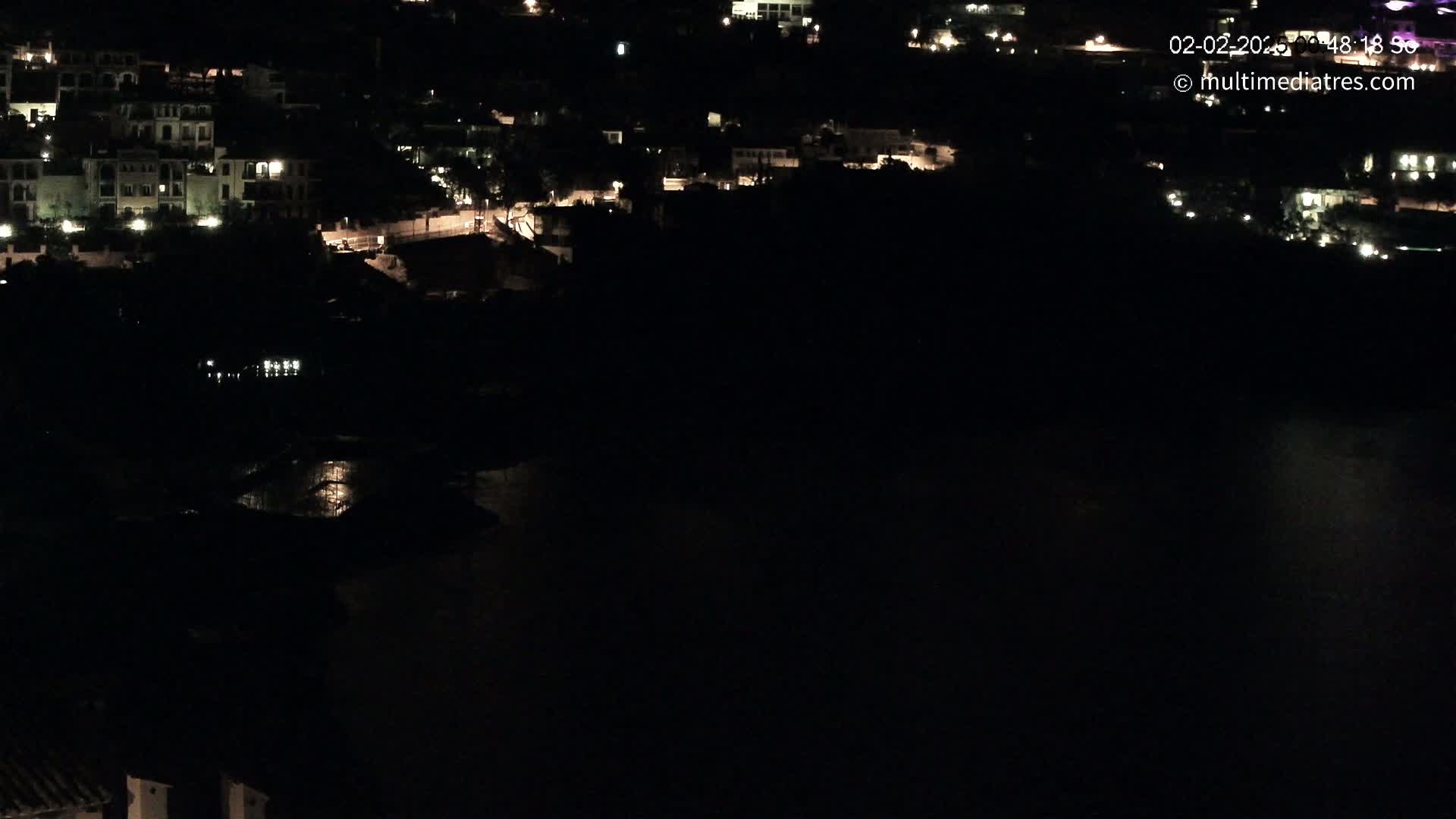A nighttime view of a coastal town with scattered lights visible against a dark body of water.
