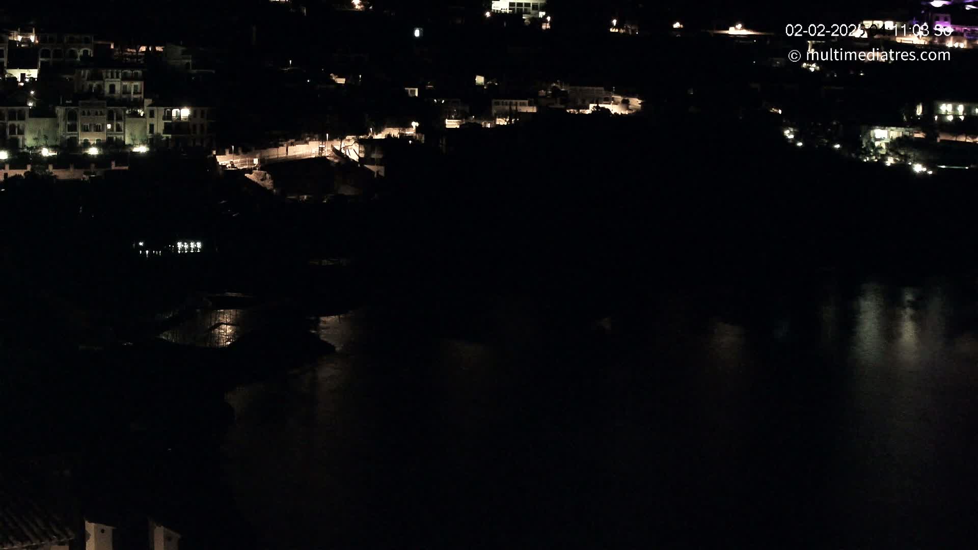 A nighttime view of a coastal town with buildings illuminated along a dark body of water.
