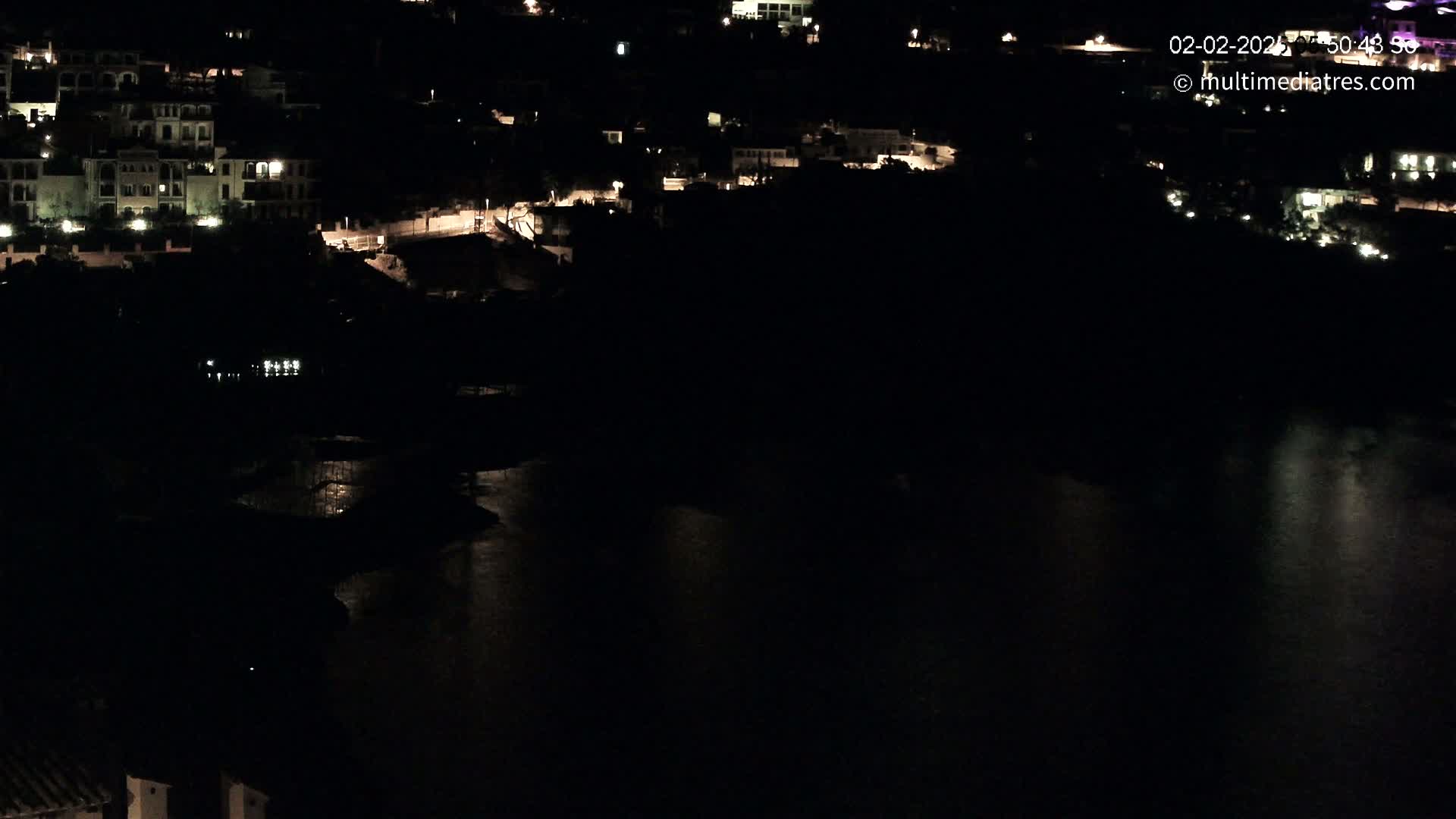 A nighttime view of a coastal town with buildings illuminated along a dark body of water.