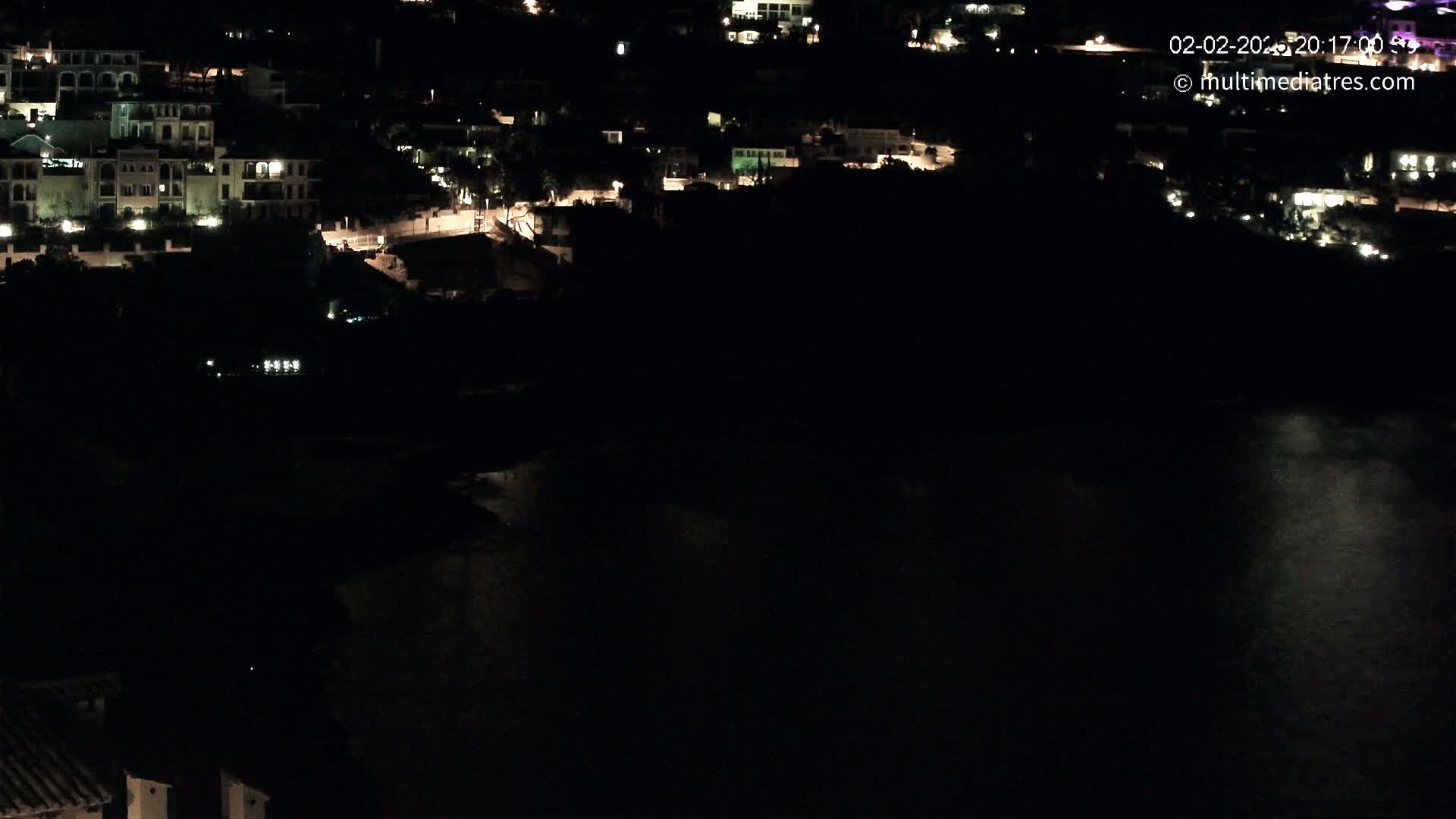 A nighttime view of a coastal town with dimly lit buildings and a dark body of water.