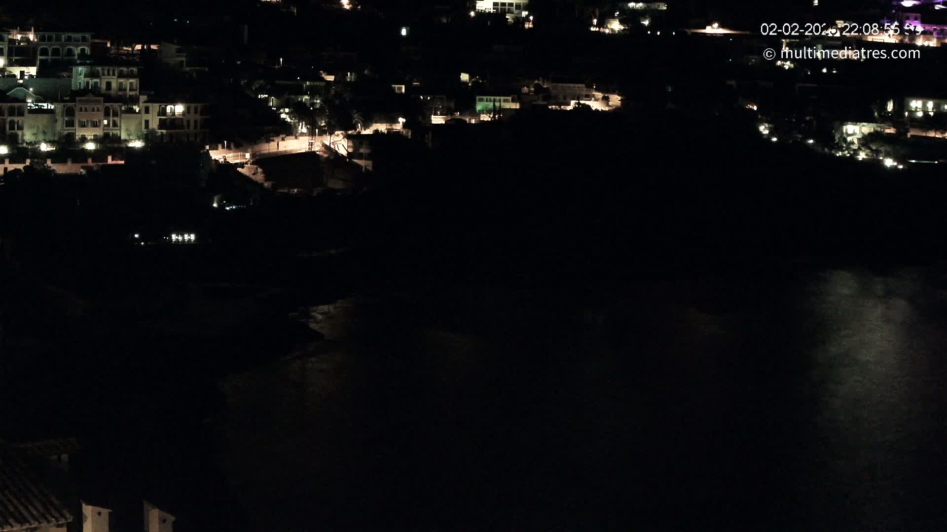A nighttime view of a coastal town with buildings illuminated, overlooking a dark body of water.
