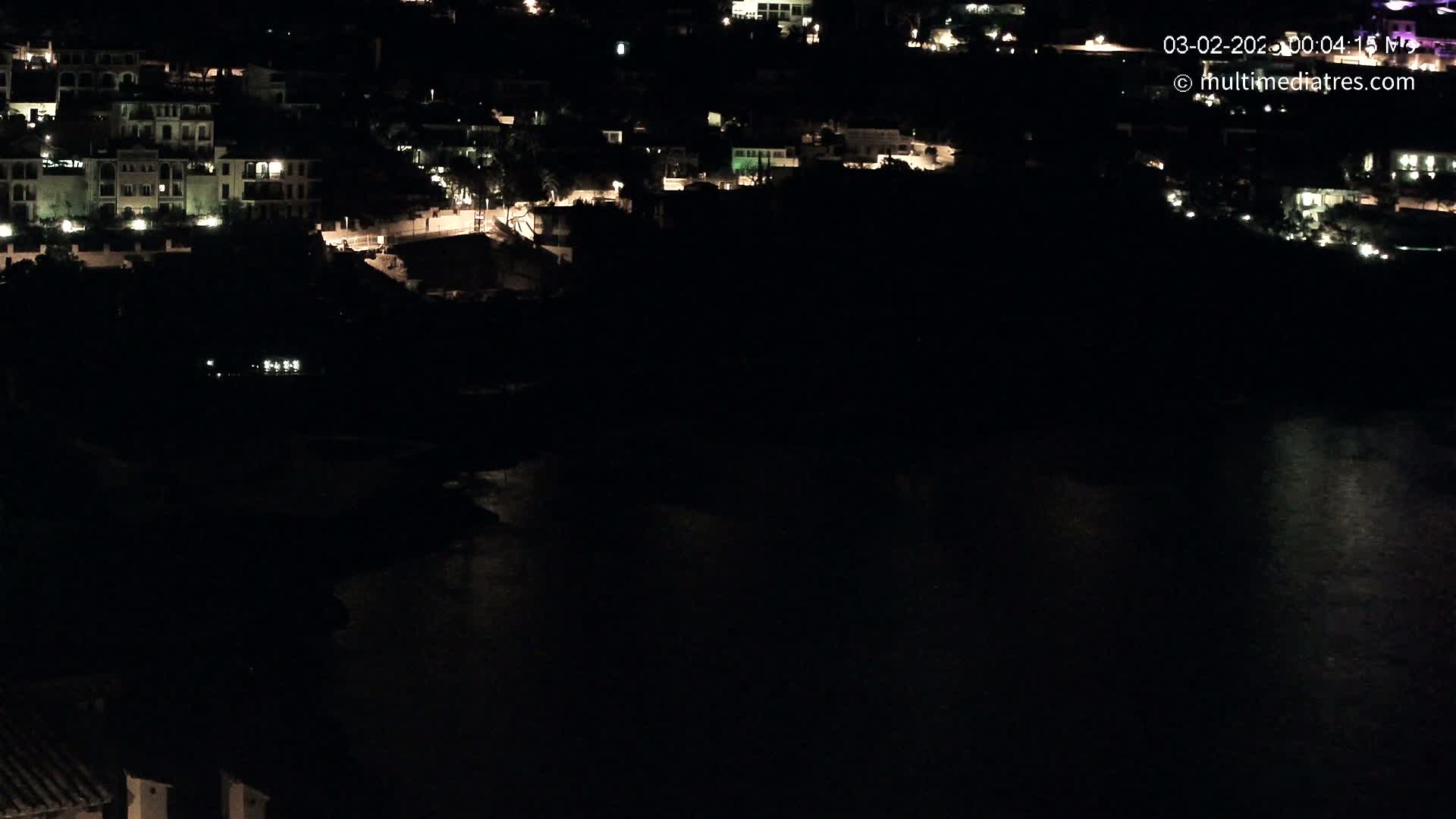 A nighttime view shows a coastal town with sparsely lit buildings and a dark body of water below.