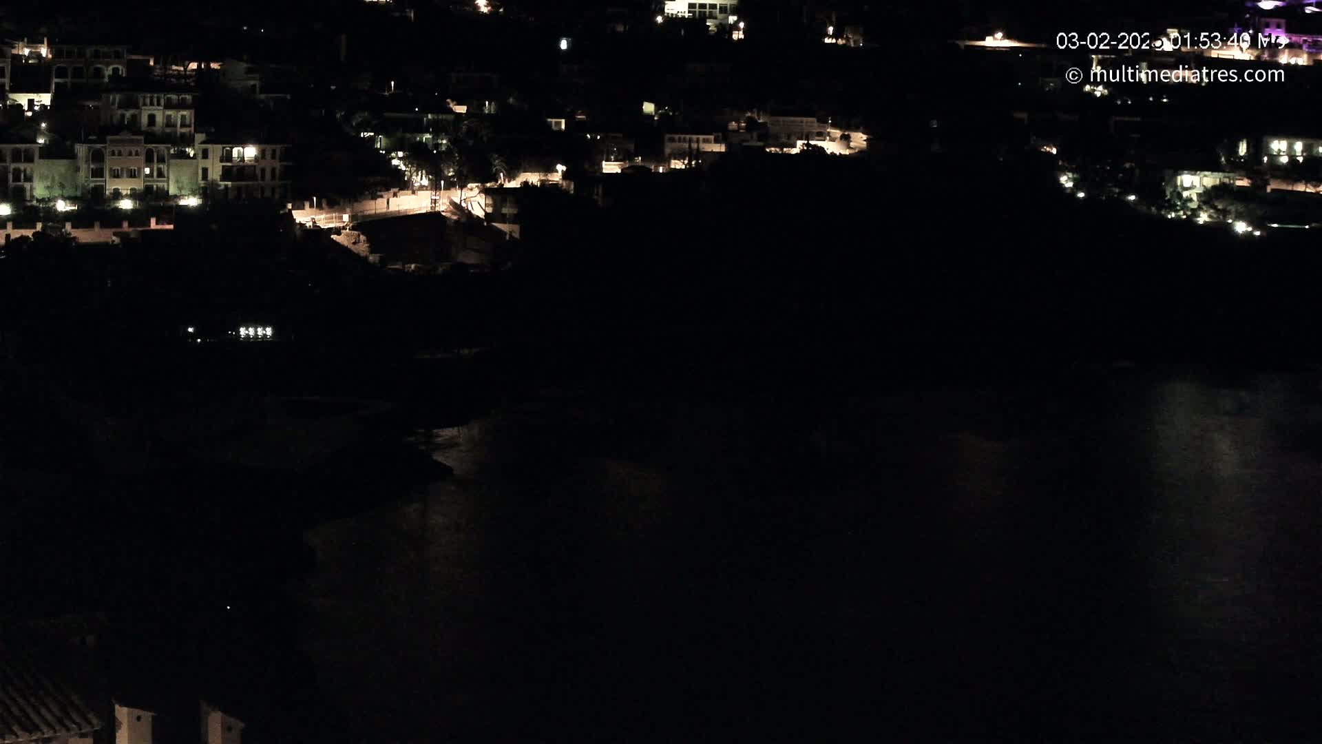 A nighttime view of a coastal town with dimly lit buildings and a dark body of water below.
