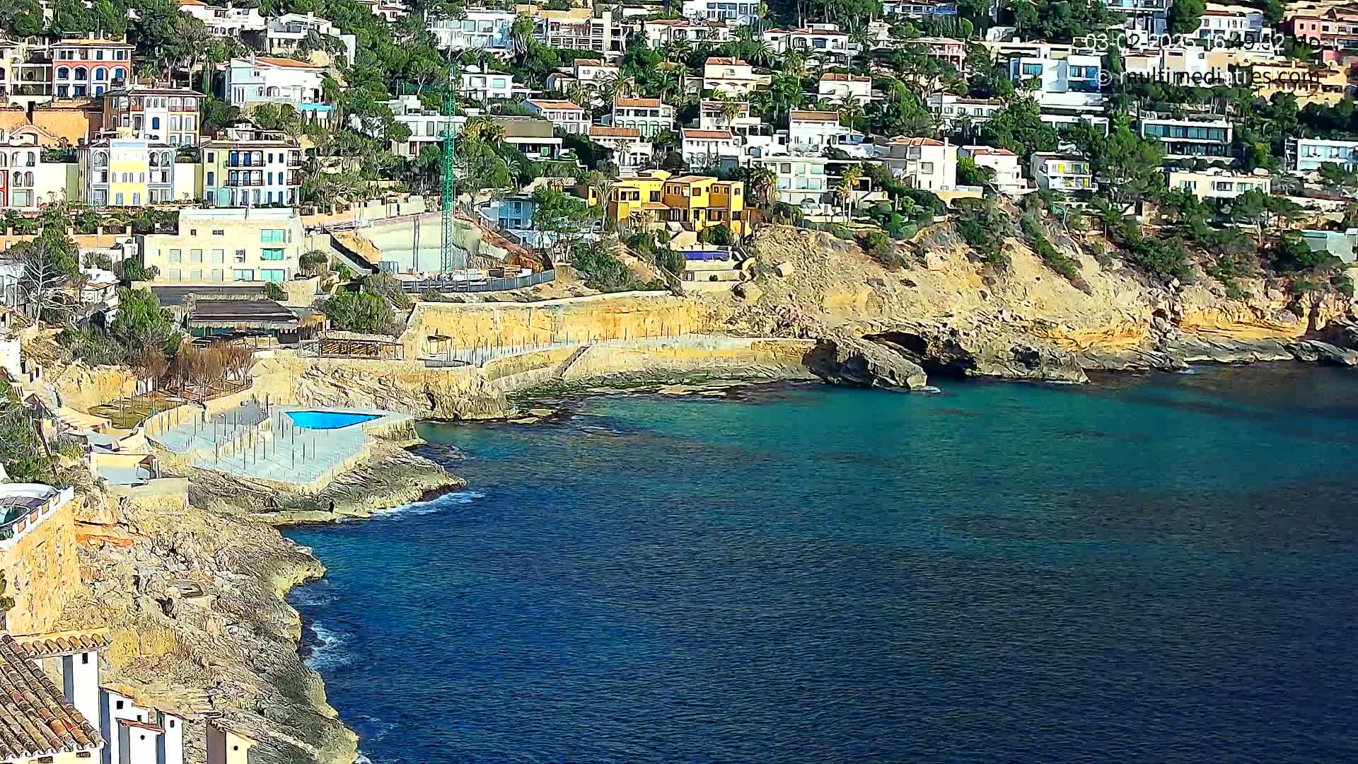 A coastal town with many houses built into a hillside overlooking a calm, teal-colored sea.
