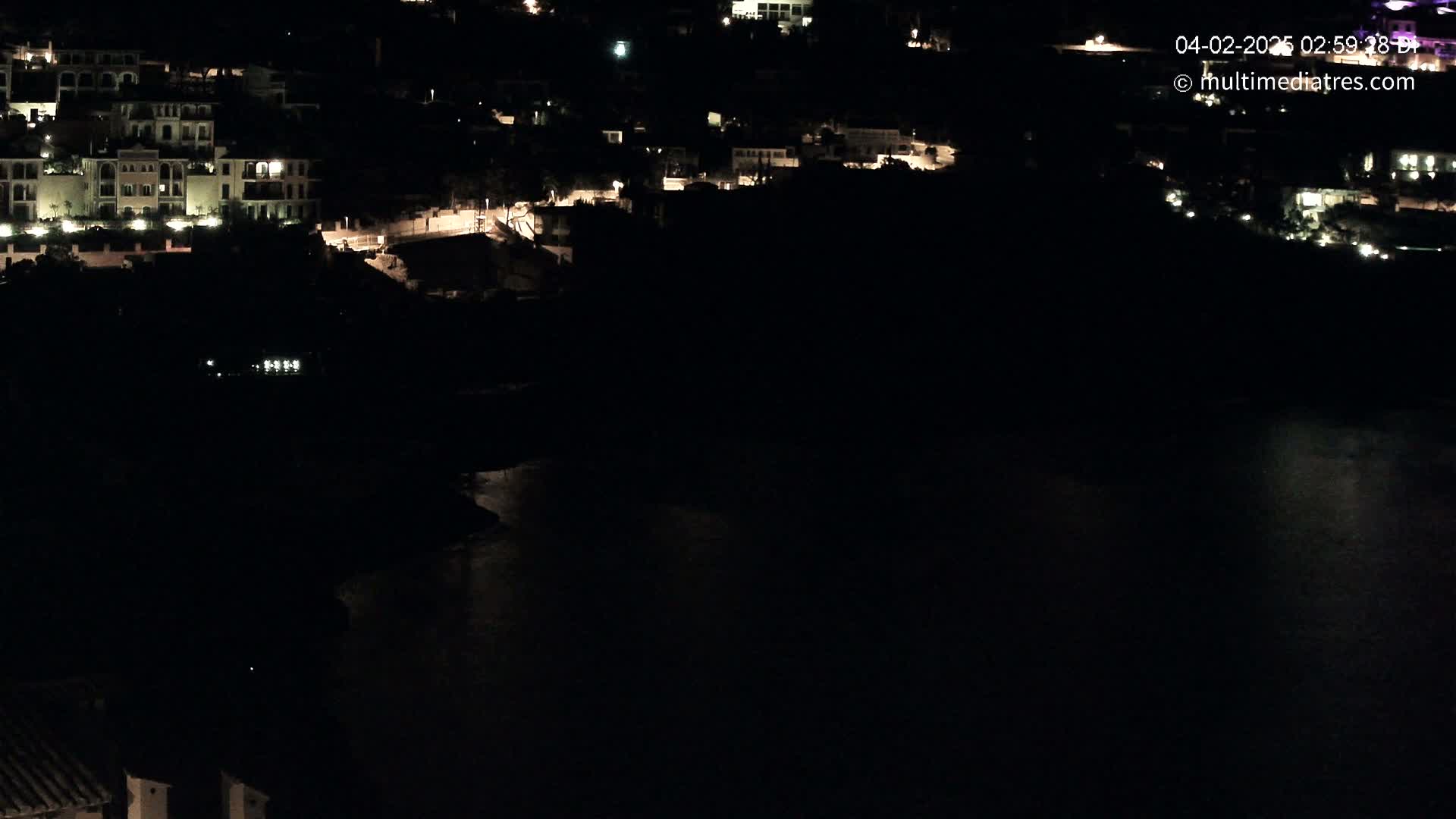 A nighttime view of a coastal town with illuminated buildings overlooking a dark body of water.