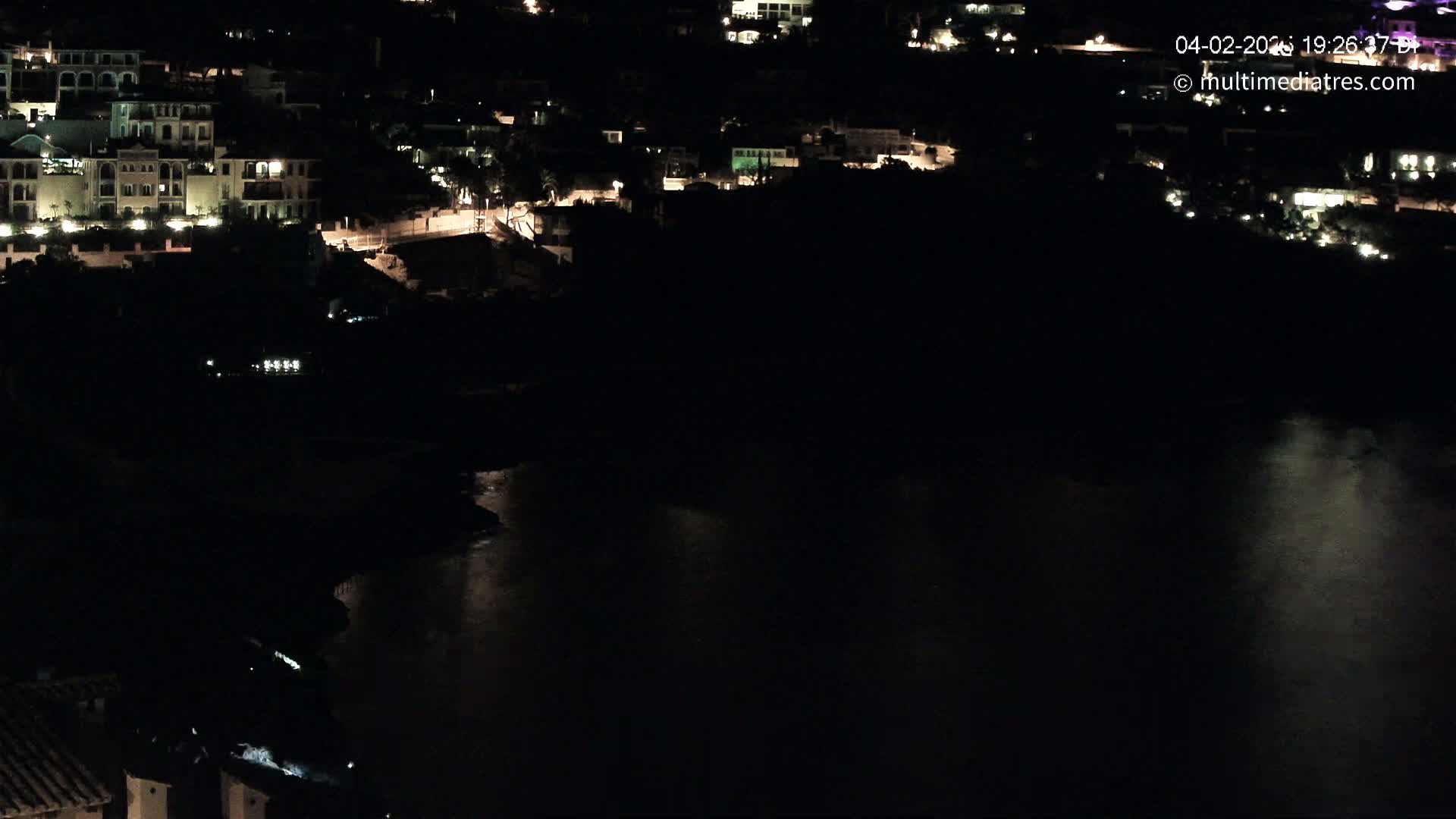 A nighttime view of a dark body of water reflecting light from a nearby town with illuminated buildings.