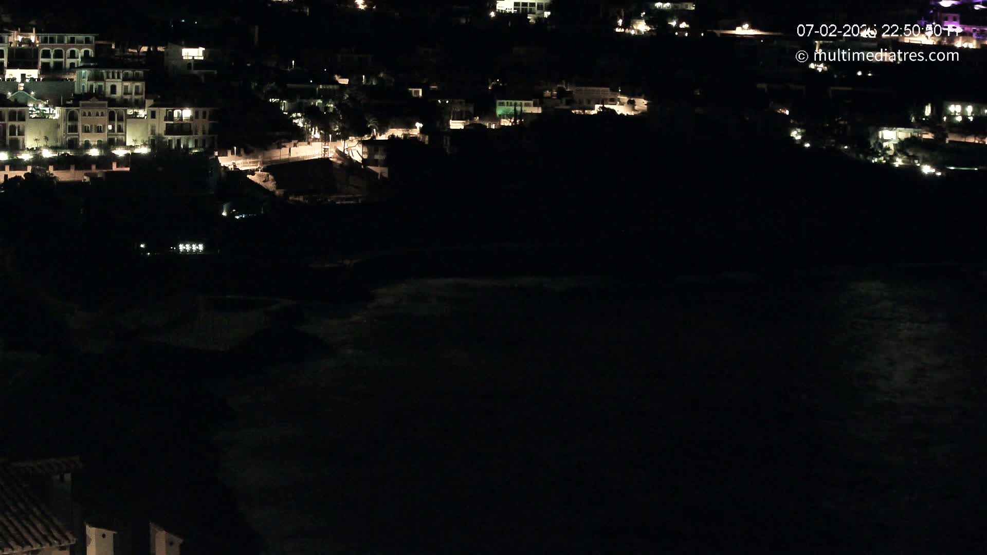 A nighttime view of a coastal town with buildings lit up along a dark body of water.