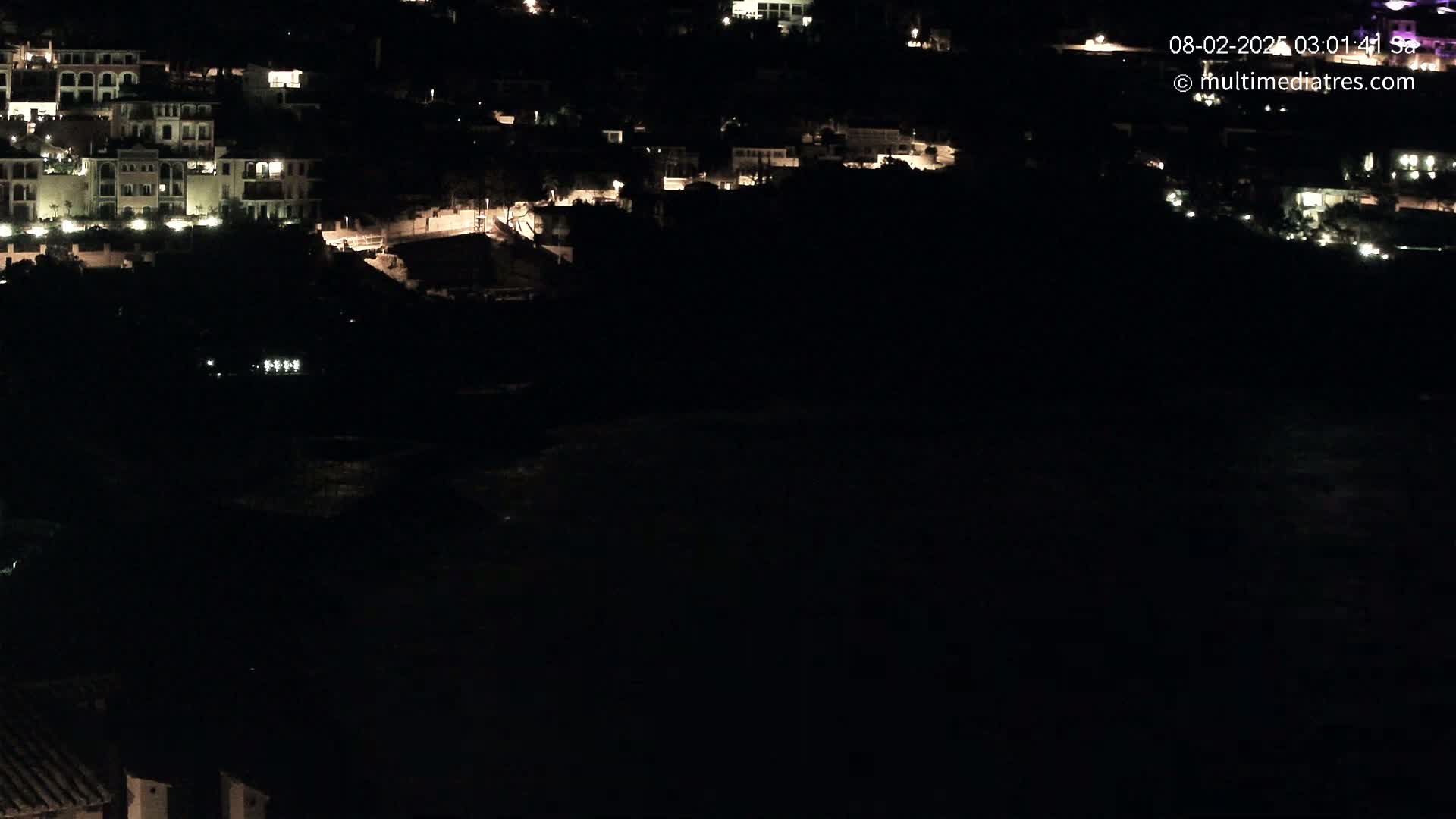 A nighttime view of a coastal town with dimly lit buildings overlooking a dark body of water.