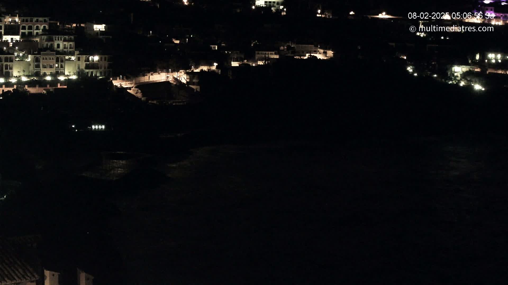 A nighttime, long shot of a coastal town with dimly lit buildings and a dark body of water.