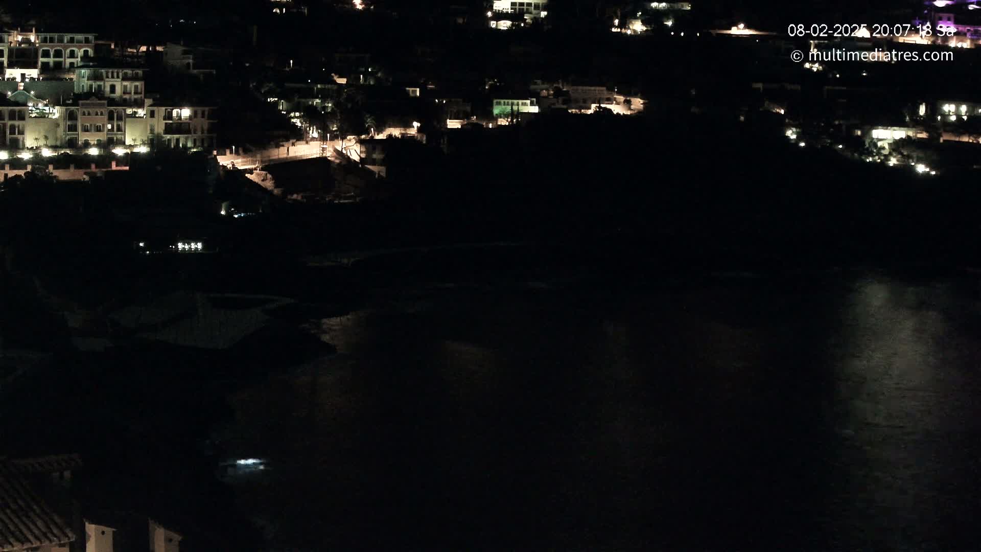 A nighttime view of a coastal town with dimly lit buildings and a dark body of water below.