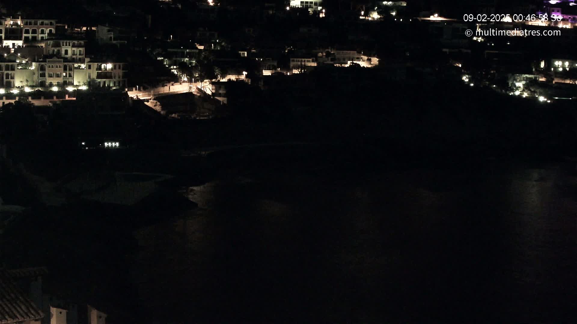 A nighttime view of a coastal town with its lights illuminated, overlooking a dark body of water.