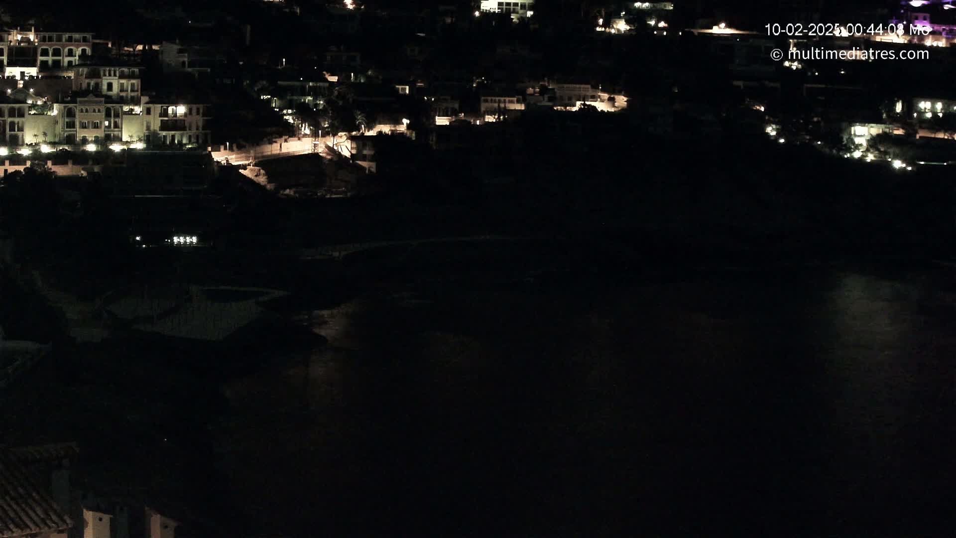 A nighttime view of a coastal town with buildings illuminated against a dark body of water.