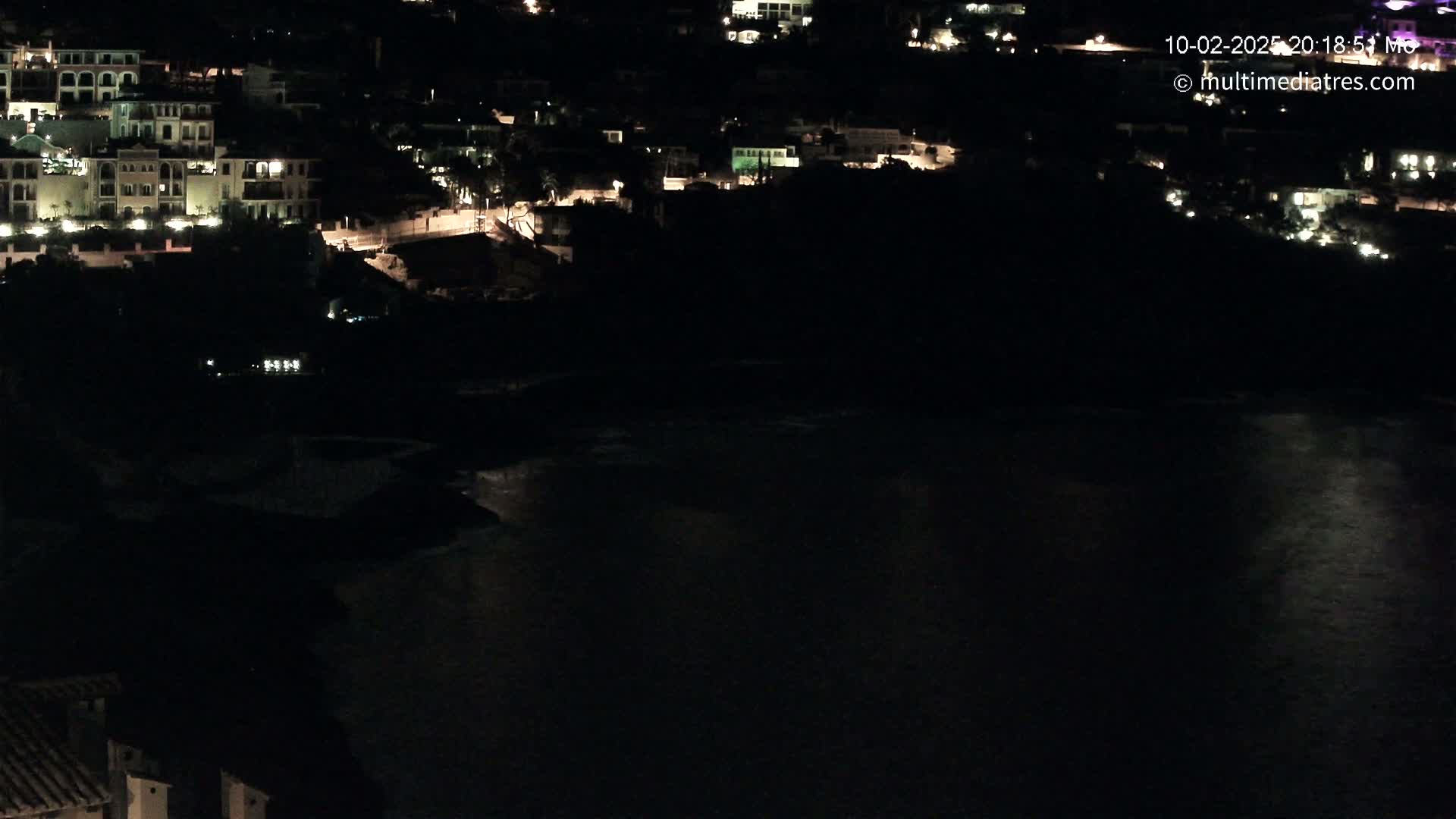 A nighttime view of a coastal town with its buildings illuminated, overlooking a dark body of water.