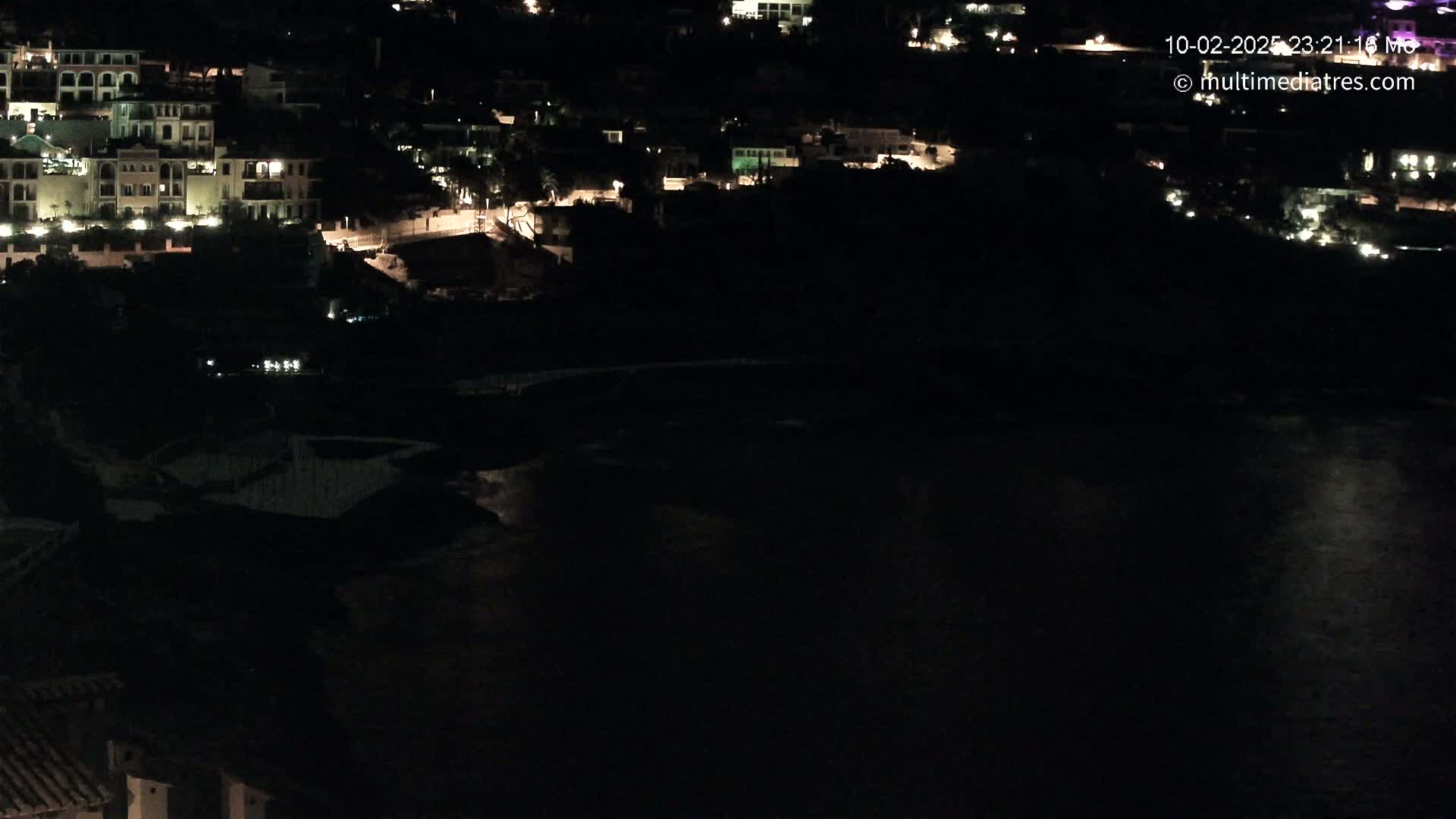 A nighttime view of a coastal town with dimly lit buildings overlooking a dark body of water.