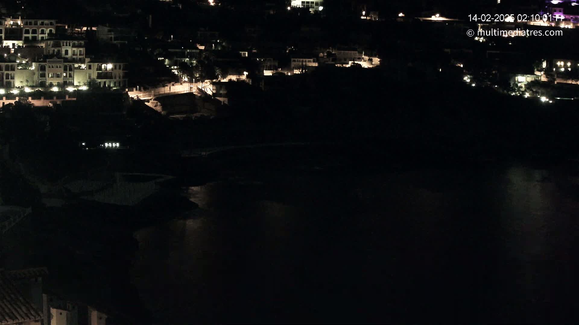 A nighttime view of a coastal town with buildings illuminated along a dark body of water.