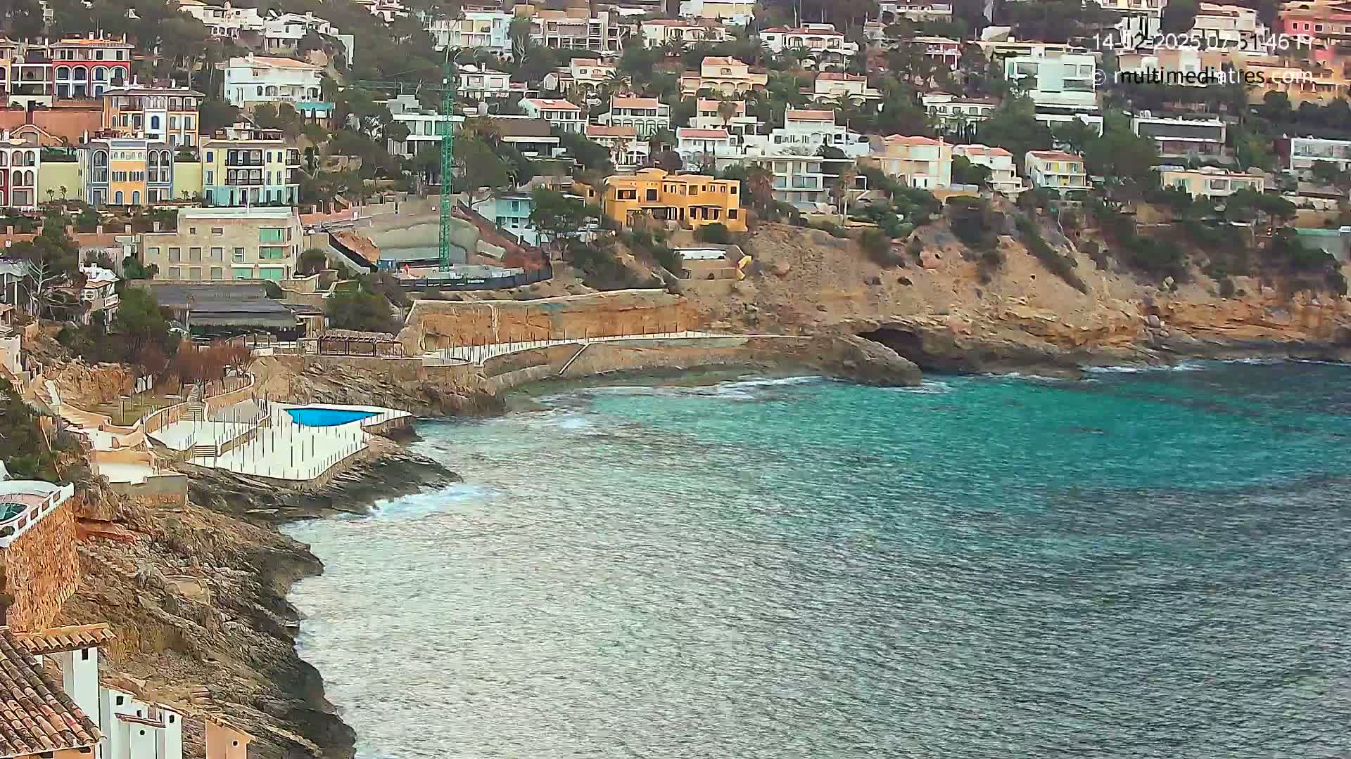 A rocky coastline with colorful houses perched on a hillside overlooking a calm, teal sea.