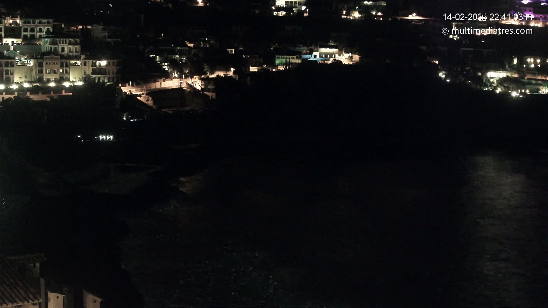 A nighttime view of a coastal town with dimly lit buildings and a dark body of water below.