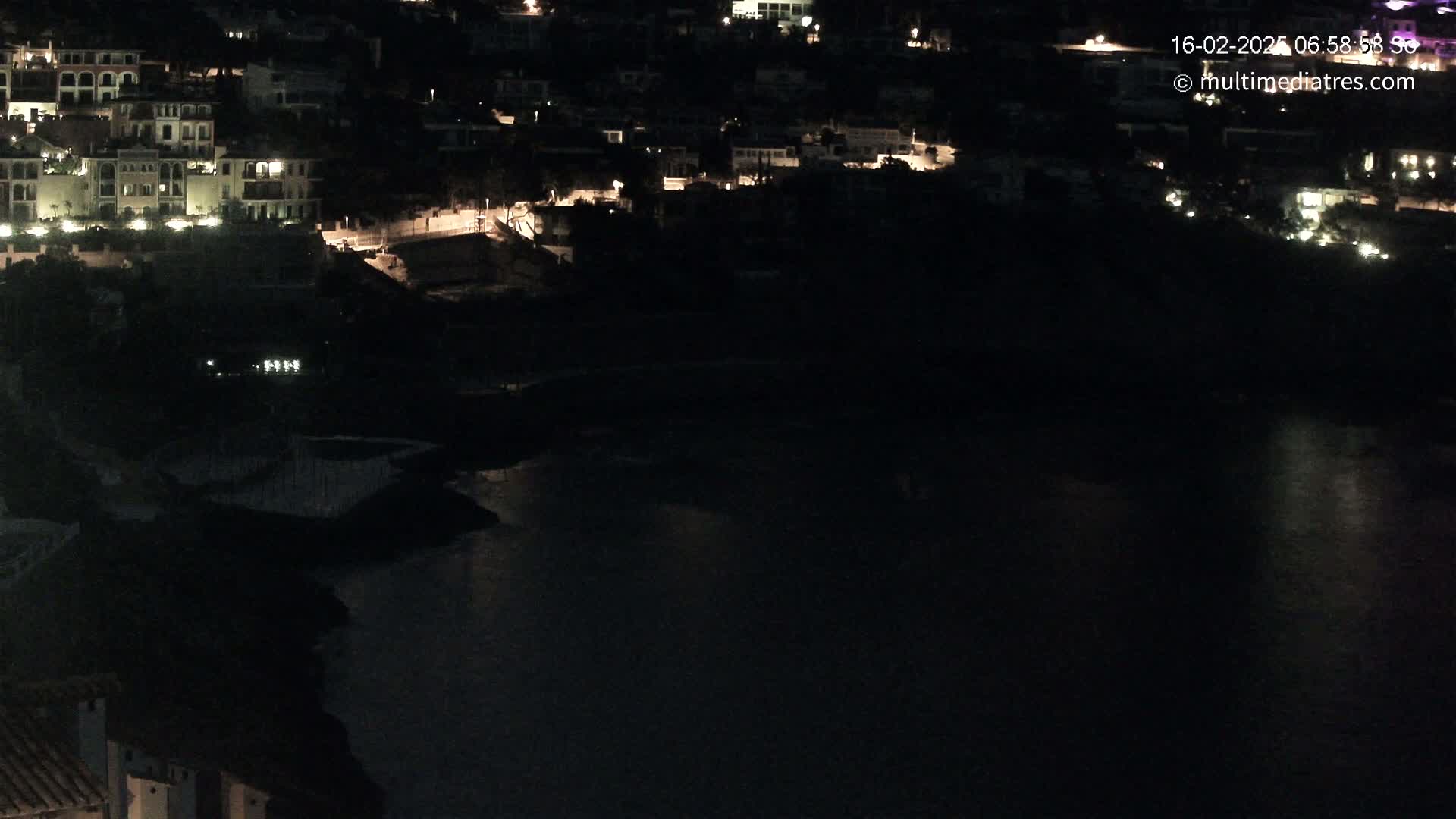 A nighttime view of a coastal town with sparsely lit buildings near a dark body of water.