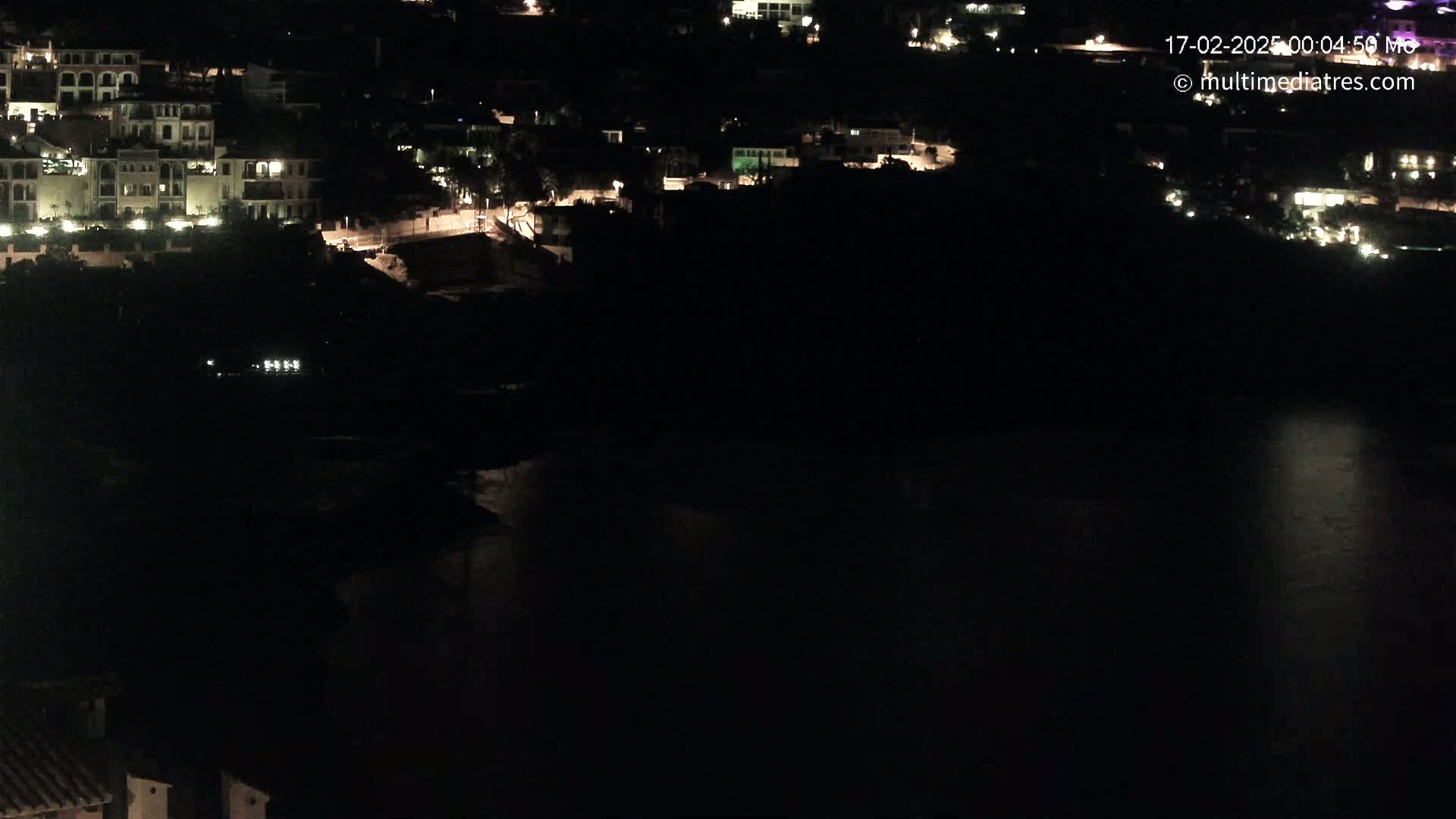 A nighttime view of a coastal town with illuminated buildings overlooking a dark body of water.